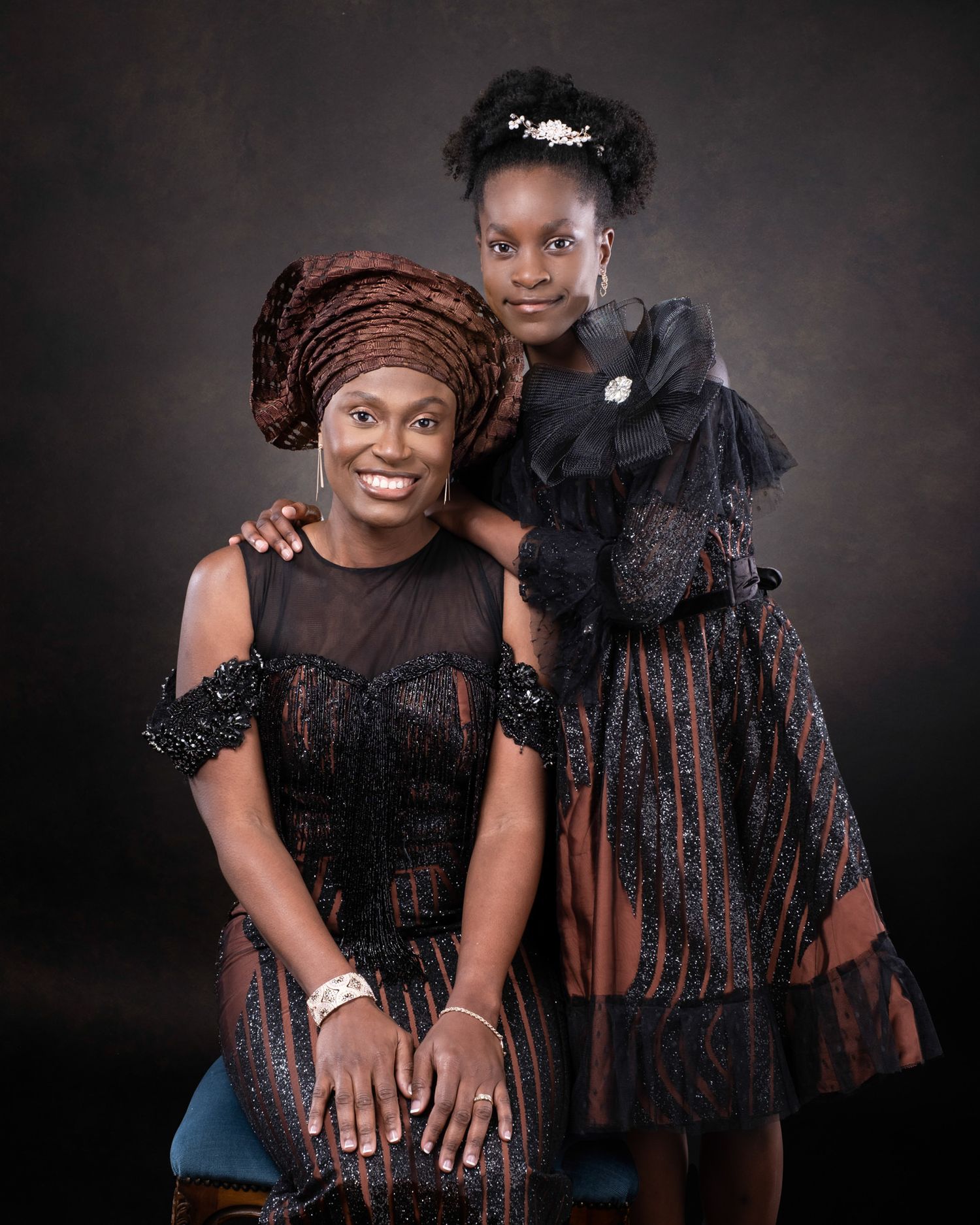 A portrait of two people wearing elegant black and brown traditional attire against a dark backdrop.