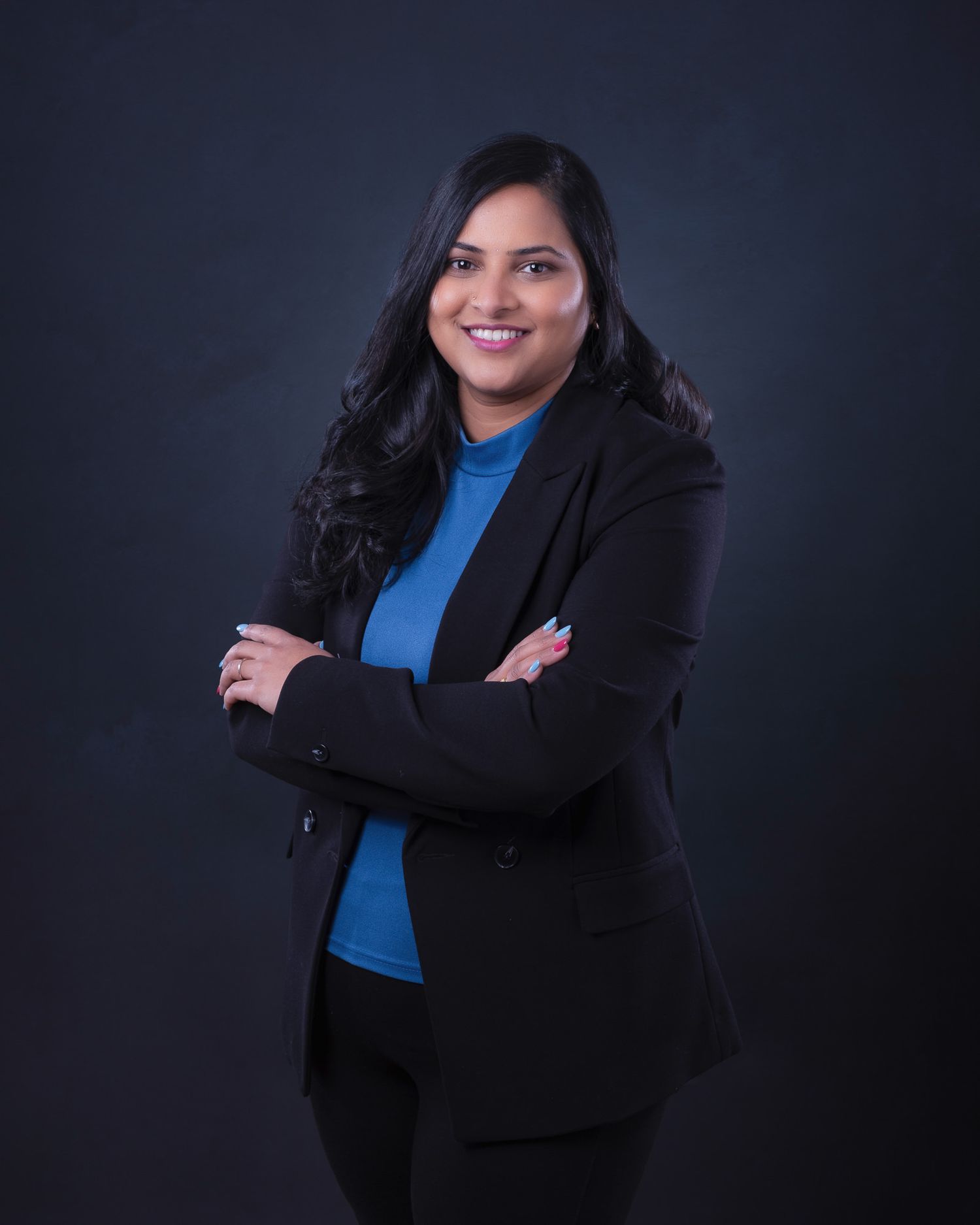 Professional in black blazer and blue top poses against dark background.