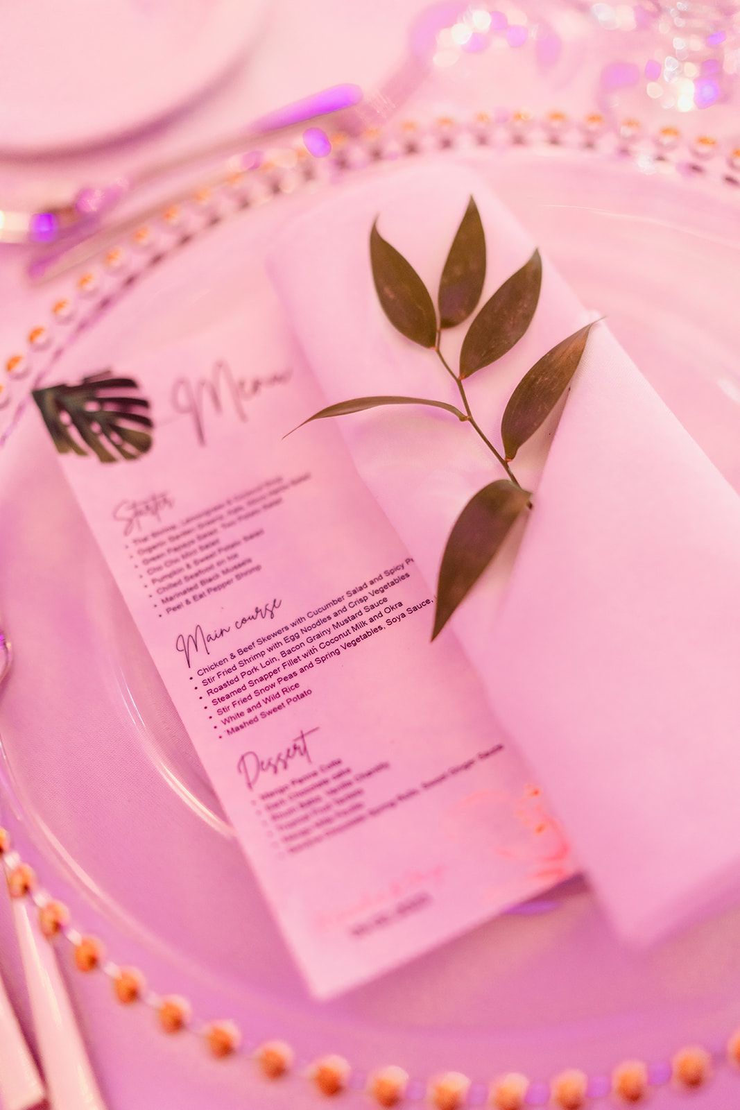 Wedding menu card with gold leaf details on pink charger plate at reception.