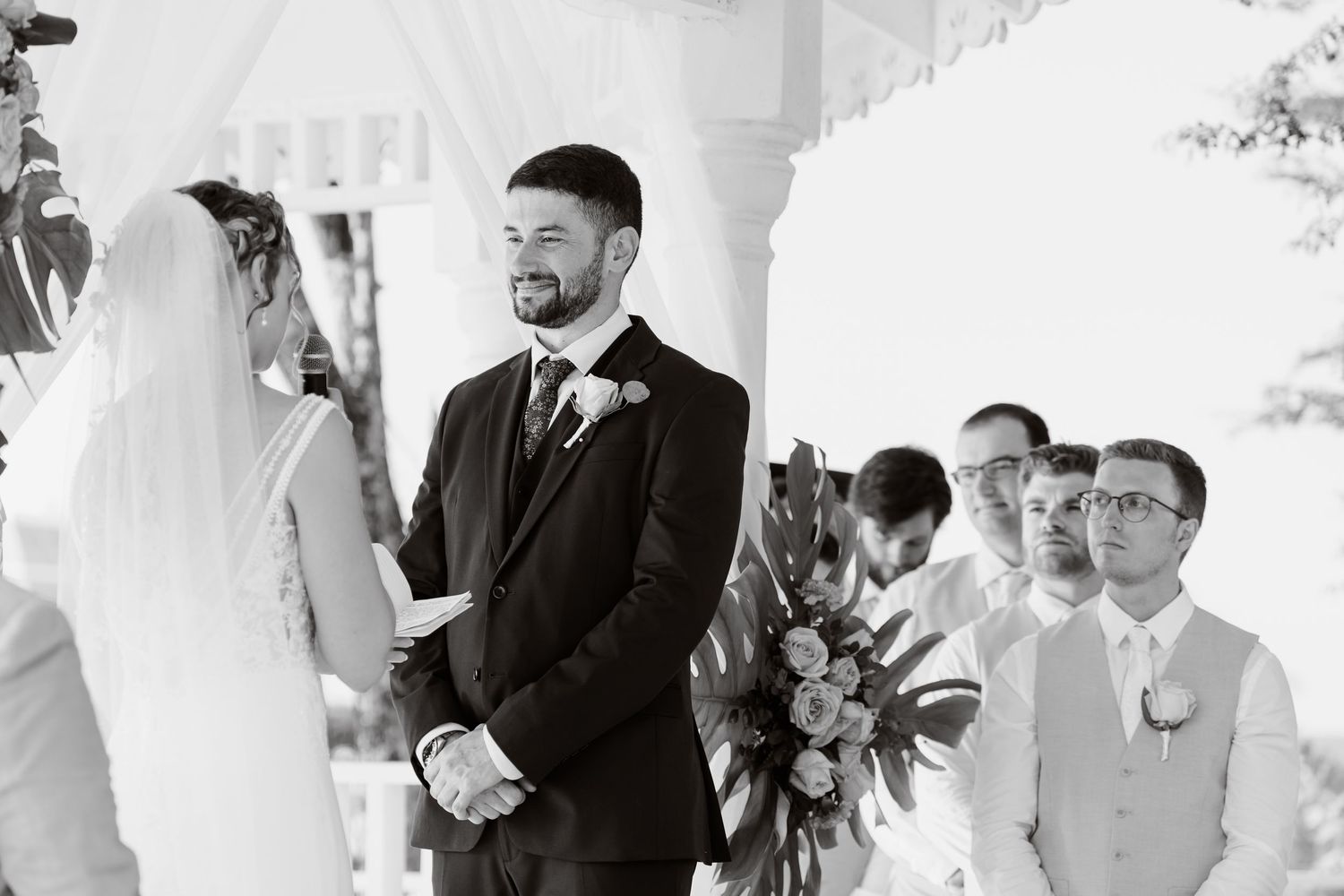 Wedding party members line up during an elegant outdoor ceremony under a white tent canopy.