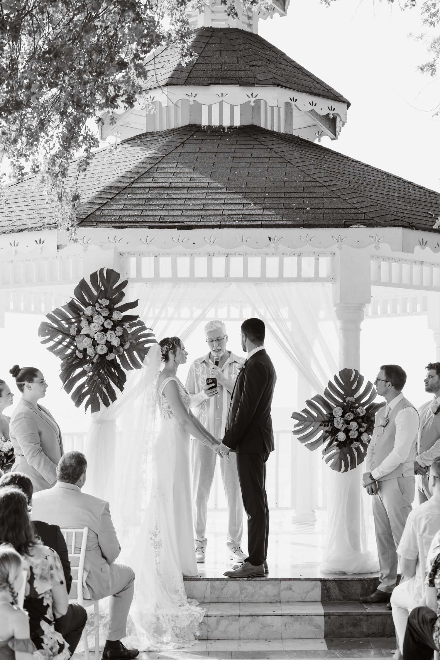 A wedding ceremony taking place inside an elegant white gazebo with monstera leaf decorations in a candid sequence.