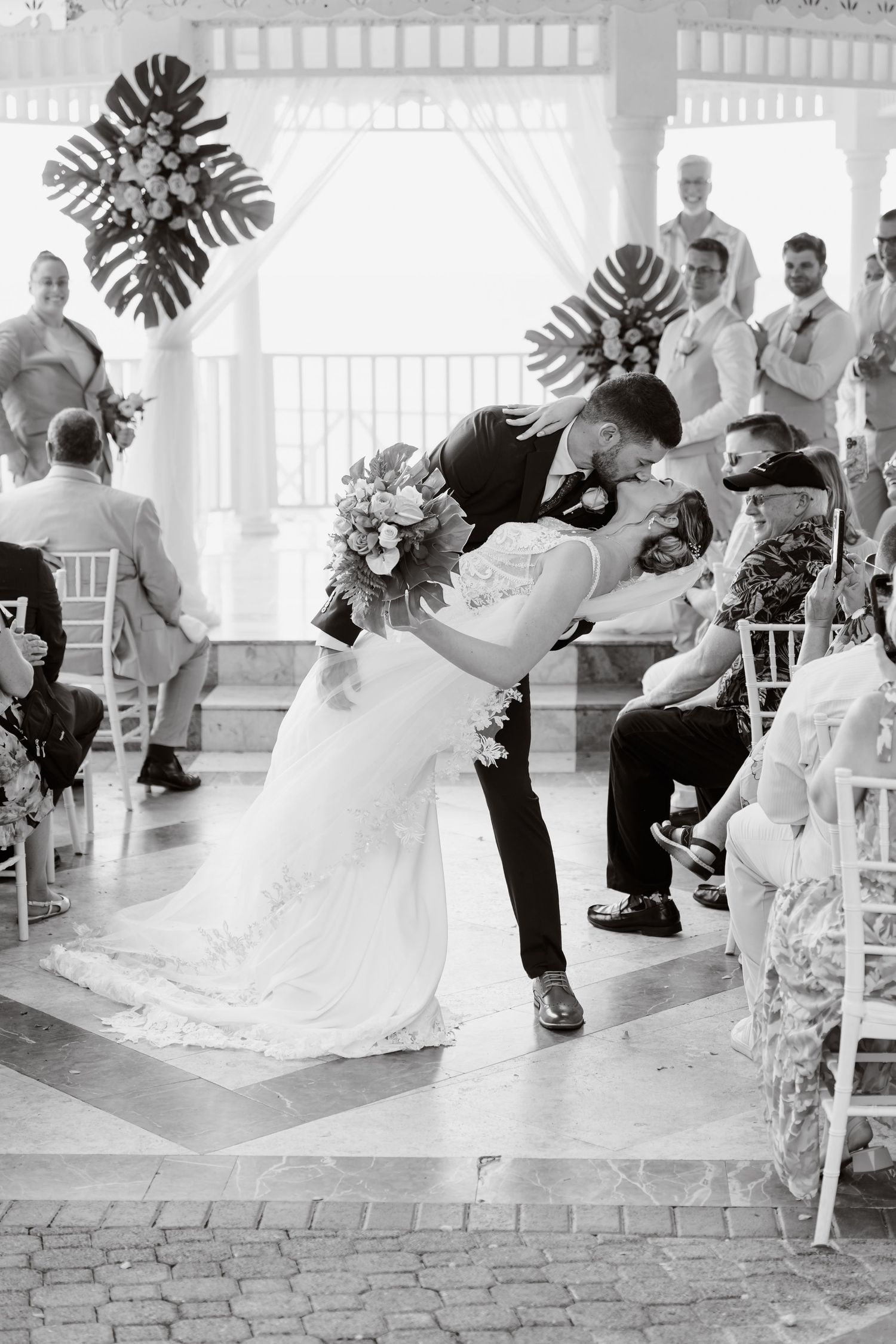 Dancing couple performs a romantic dip during their wedding celebration in a bright elegant venue with tropical decor.