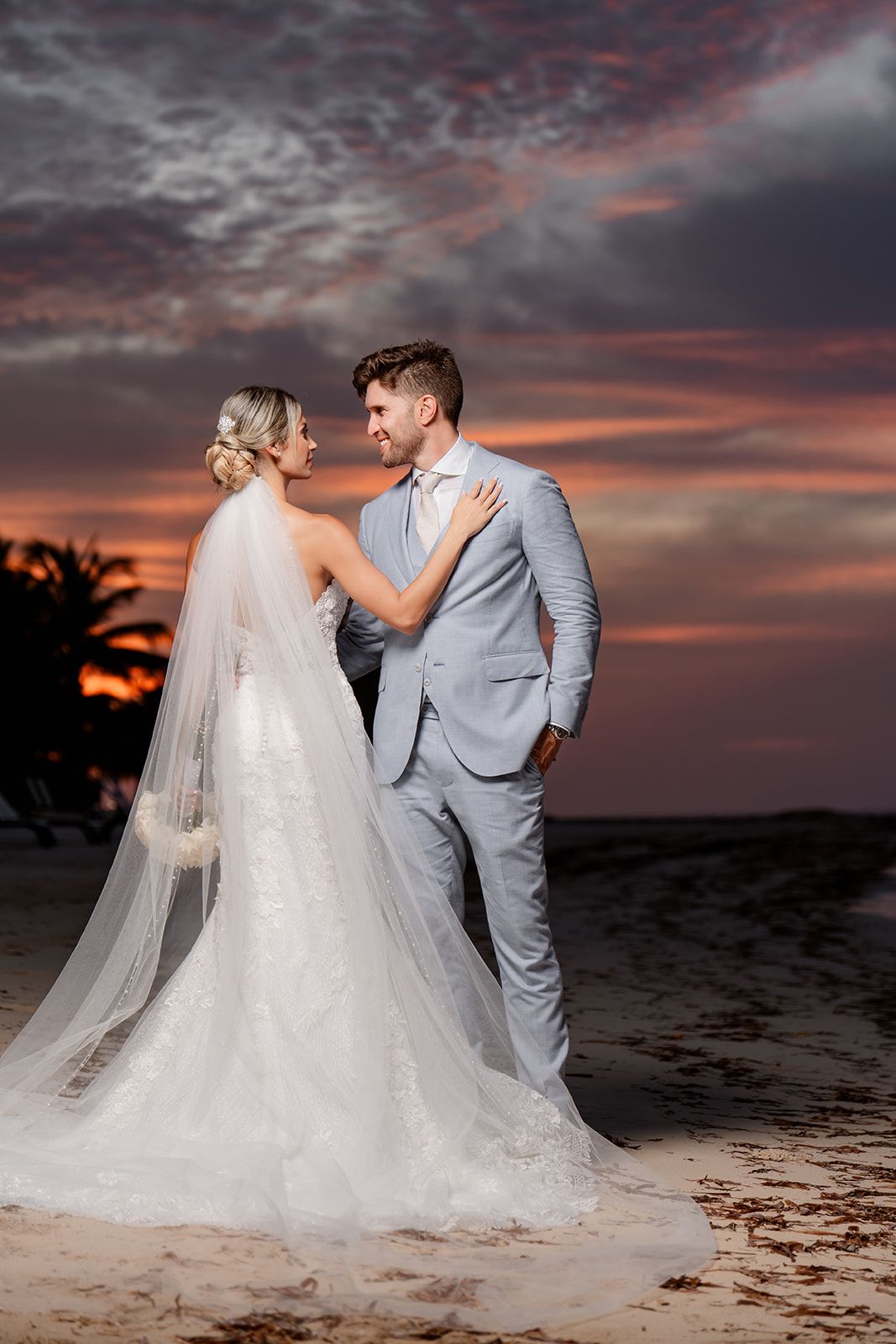 A wedding couple shares an intimate moment on the beach during sunset.