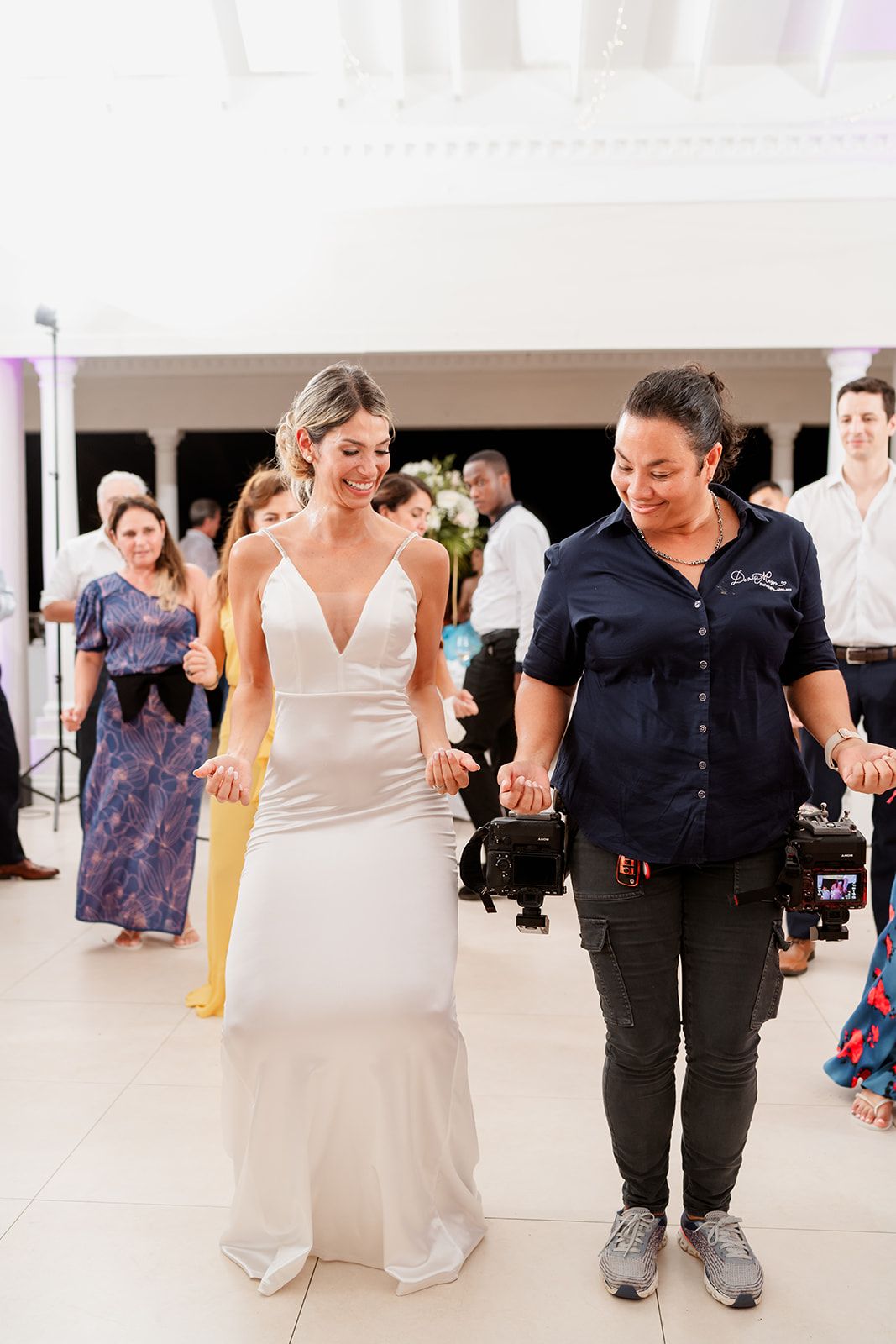 Bride in sleek white gown dances with wedding vendor at reception.