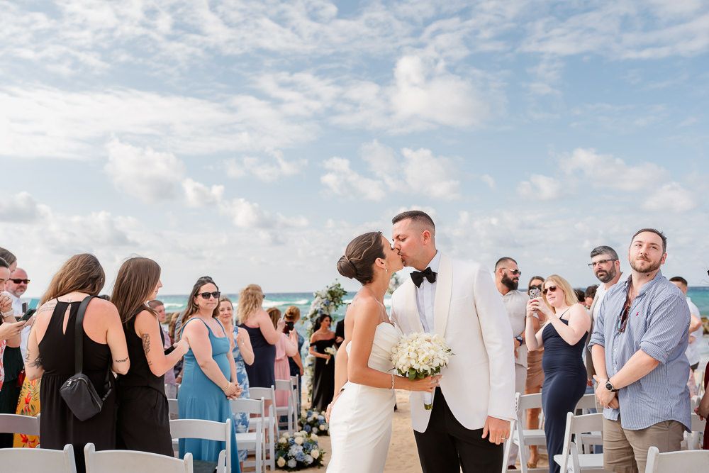 Wedding guests exchange warm hugs and greetings during an outdoor reception celebration on a sunny afternoon.