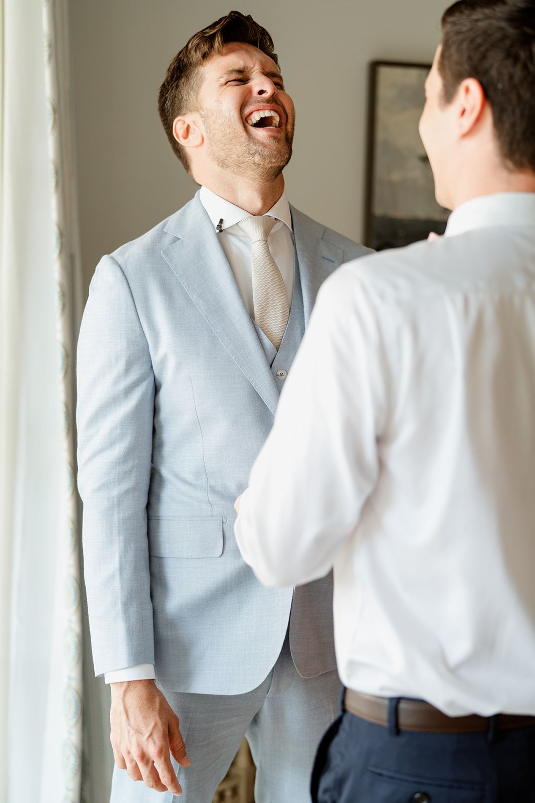 Candid moment of joyful laughter between two people during formal dressing.