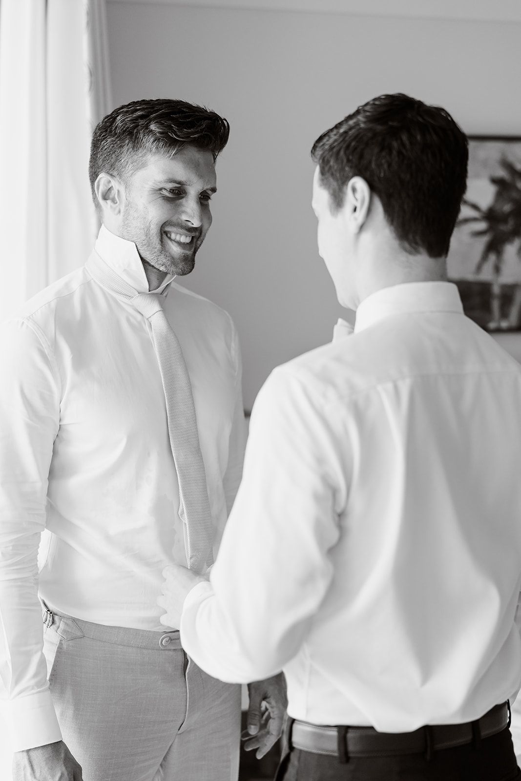 Two people sharing a candid moment while getting dressed in white shirts.