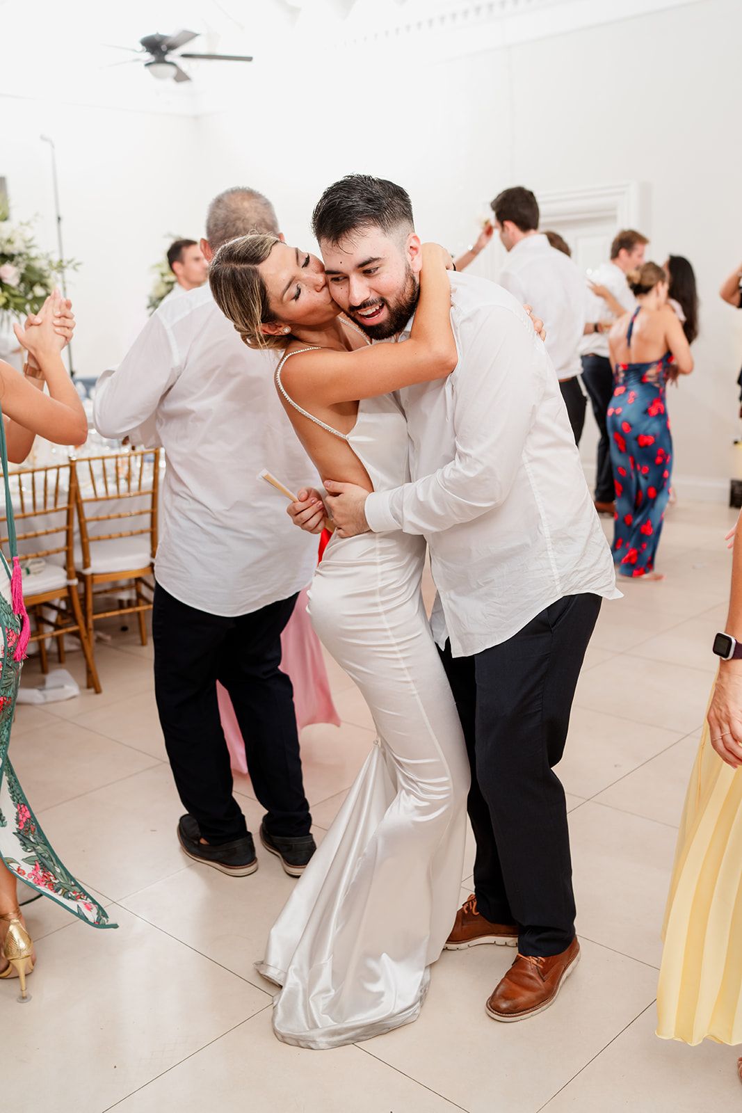 Wedding reception guests dancing and embracing in all-white attire on the dance floor.