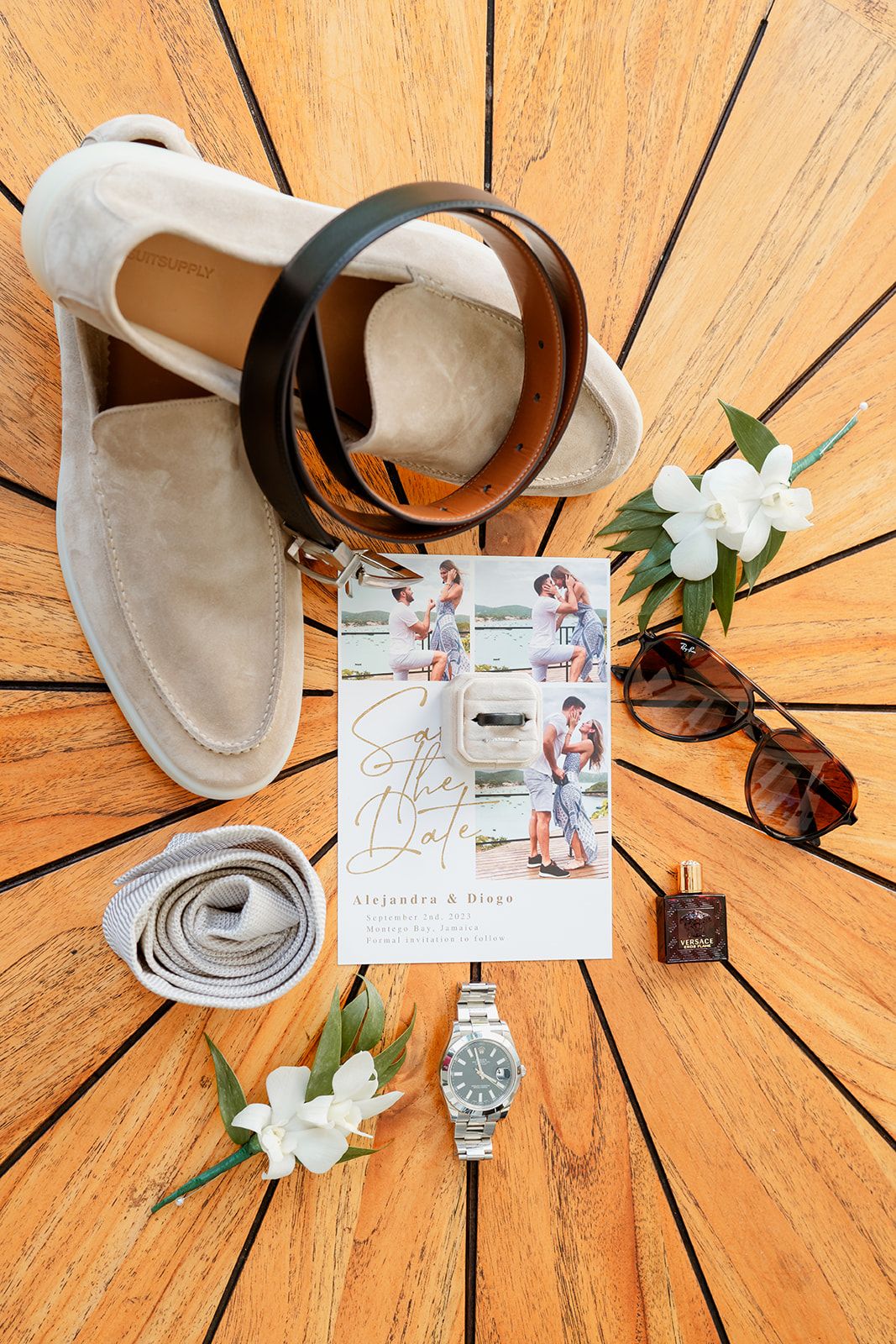 Wedding day details including shoes, invitation, sunglasses, jewelry and white flowers arranged on wooden background.