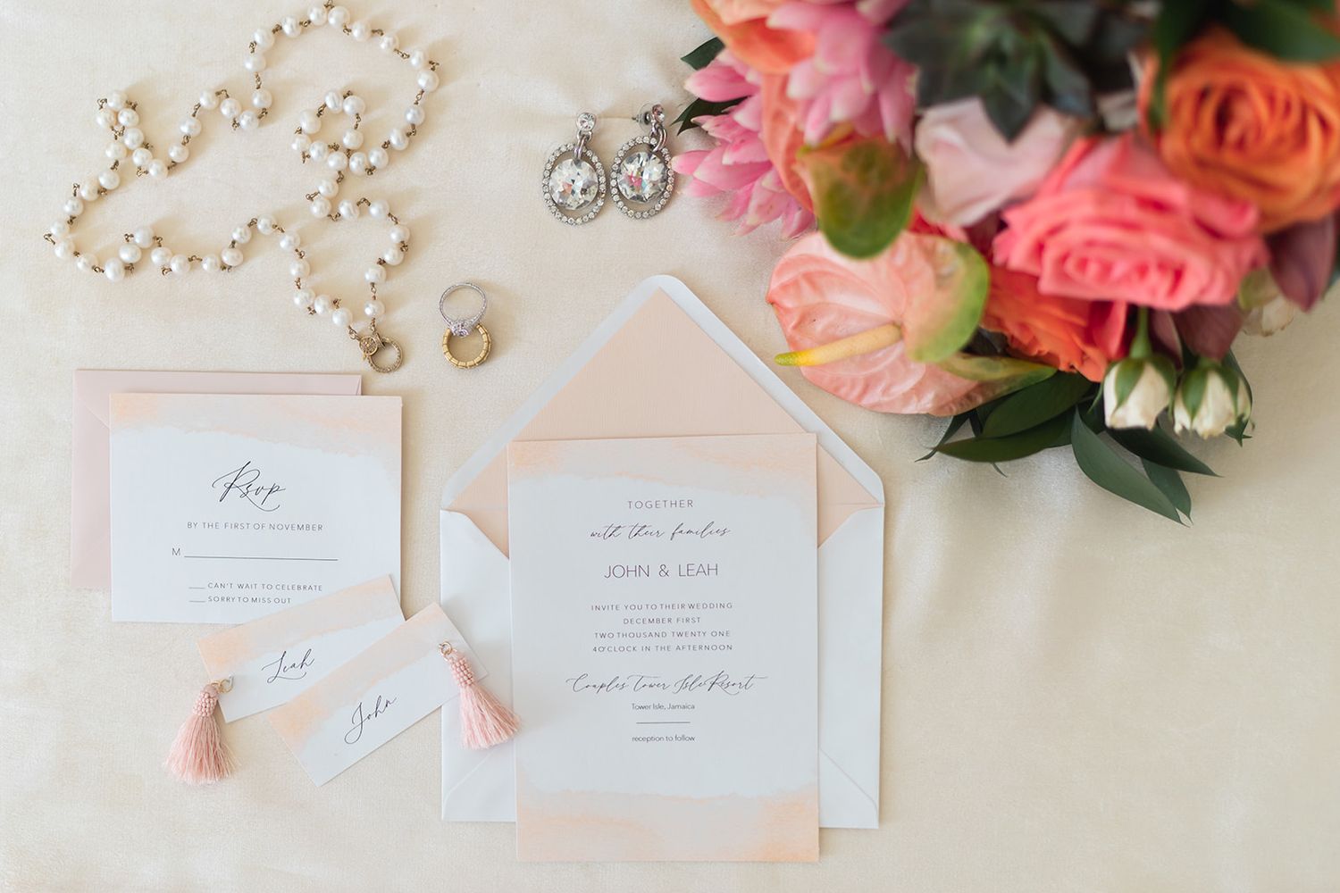 Wedding invitation suite with pearl necklace and coral roses on light background.