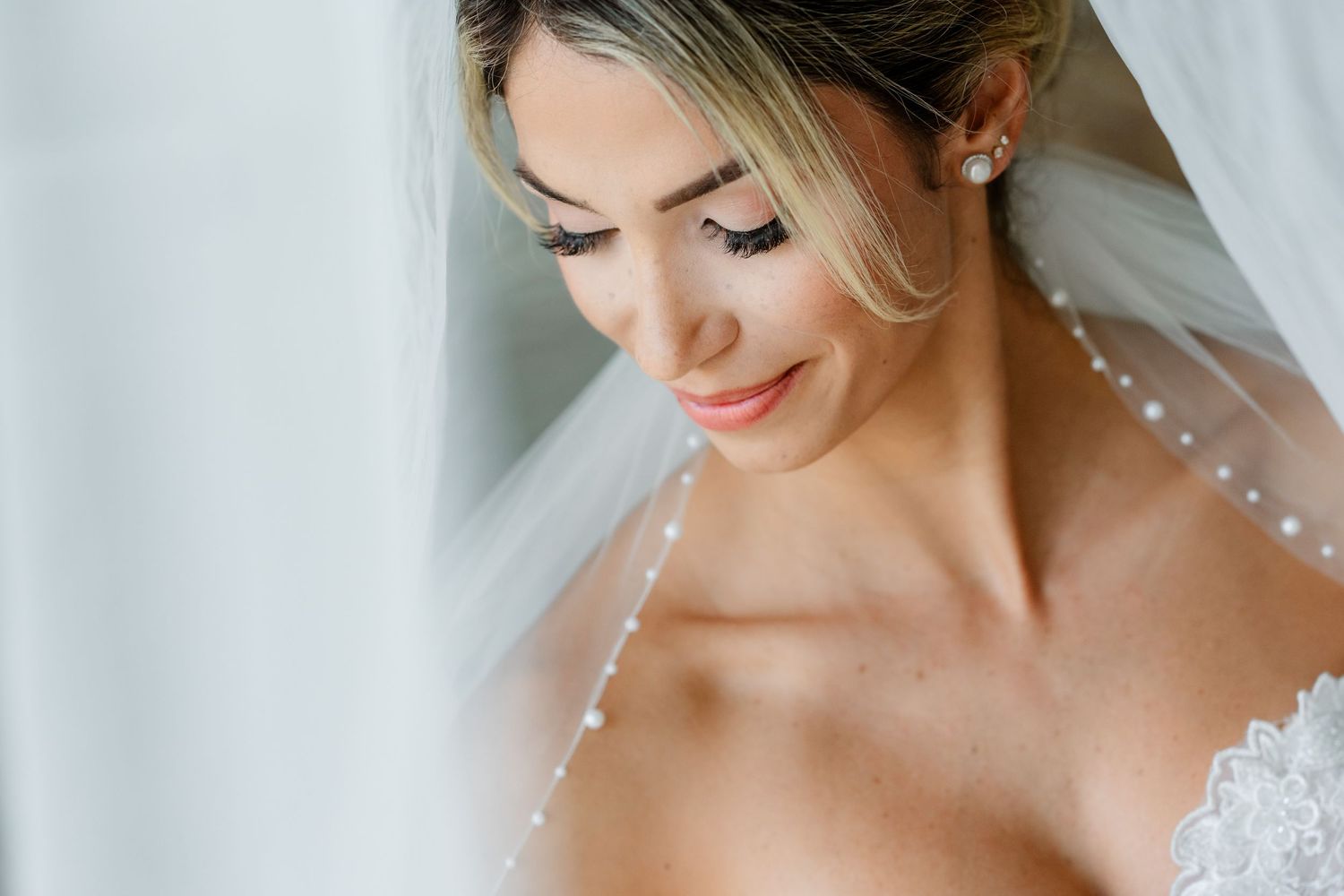Close-up portrait of bride wearing pearl-adorned veil against white background.
