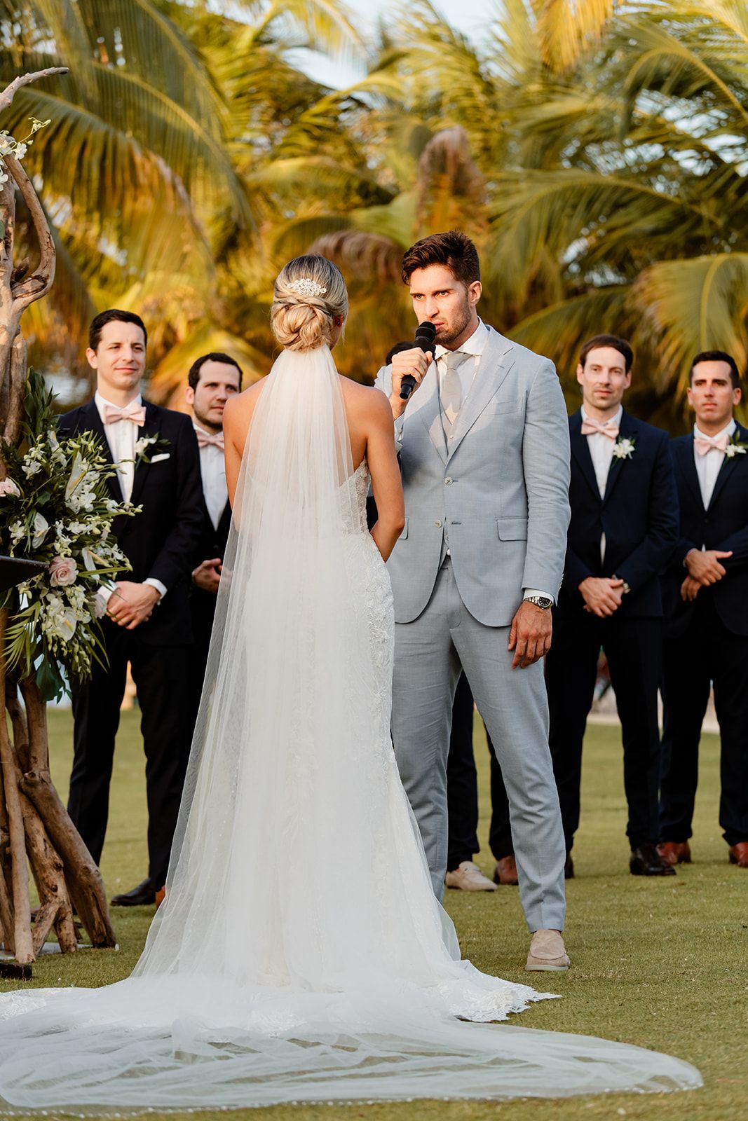 A wedding ceremony on a golf course with groomsmen in dark suits and tropical palm trees.