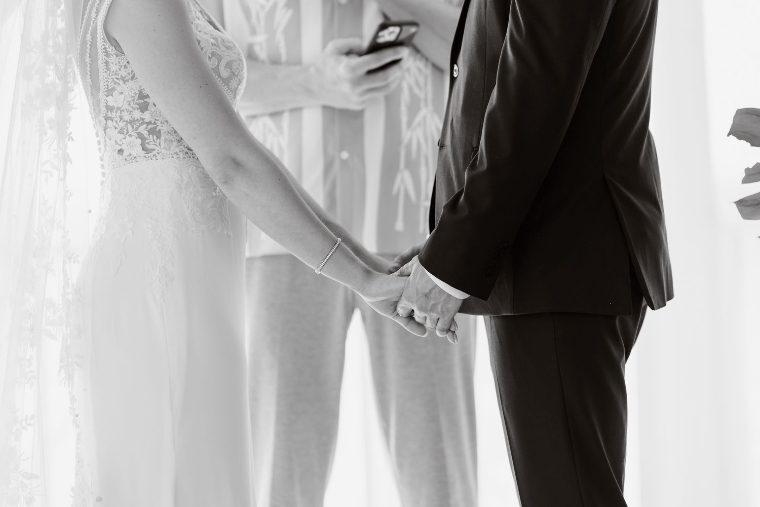 Black and white closeup photo of a bride and groom holding hands at their wedding ceremony.