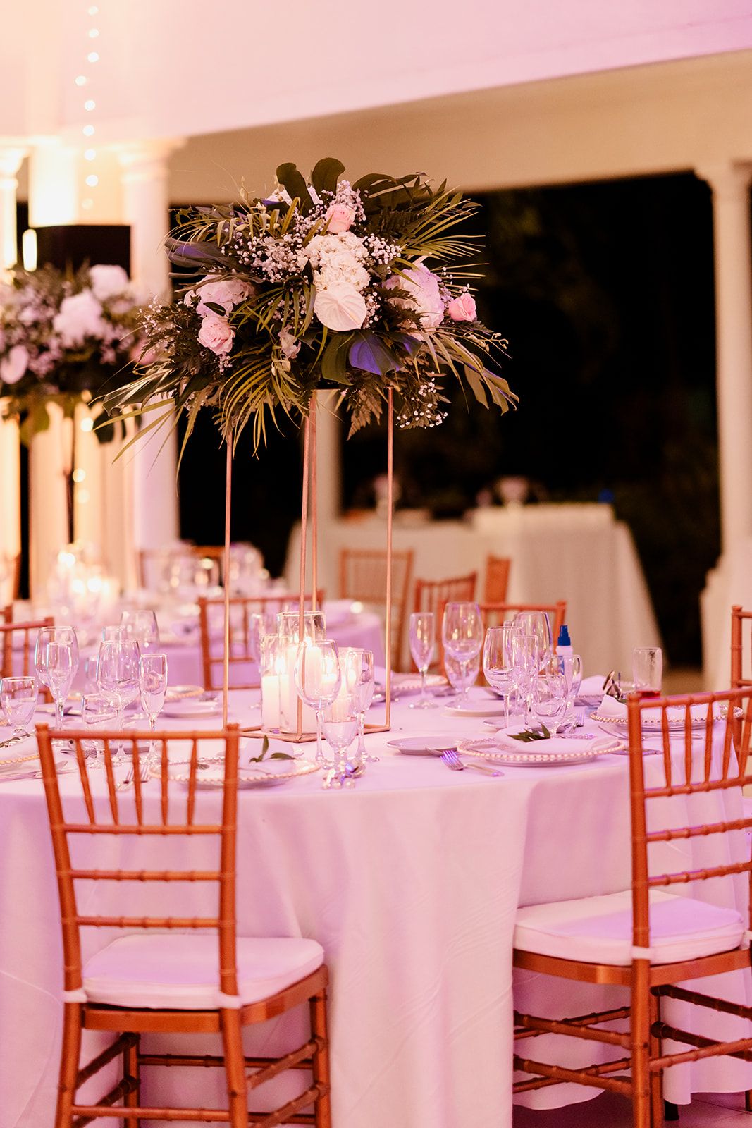 Elegant wedding reception table with tall floral centerpiece and gold chiavari chairs.