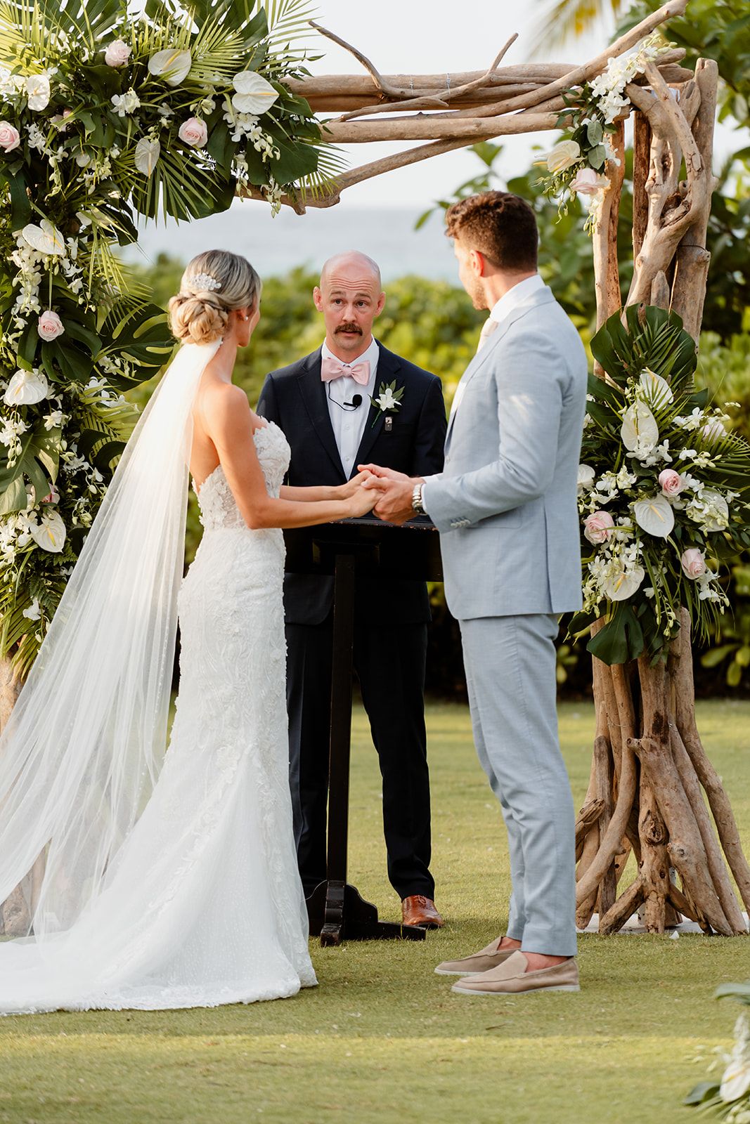 A wedding ceremony under a floral arch with white roses and greenery on a beautiful golf course.