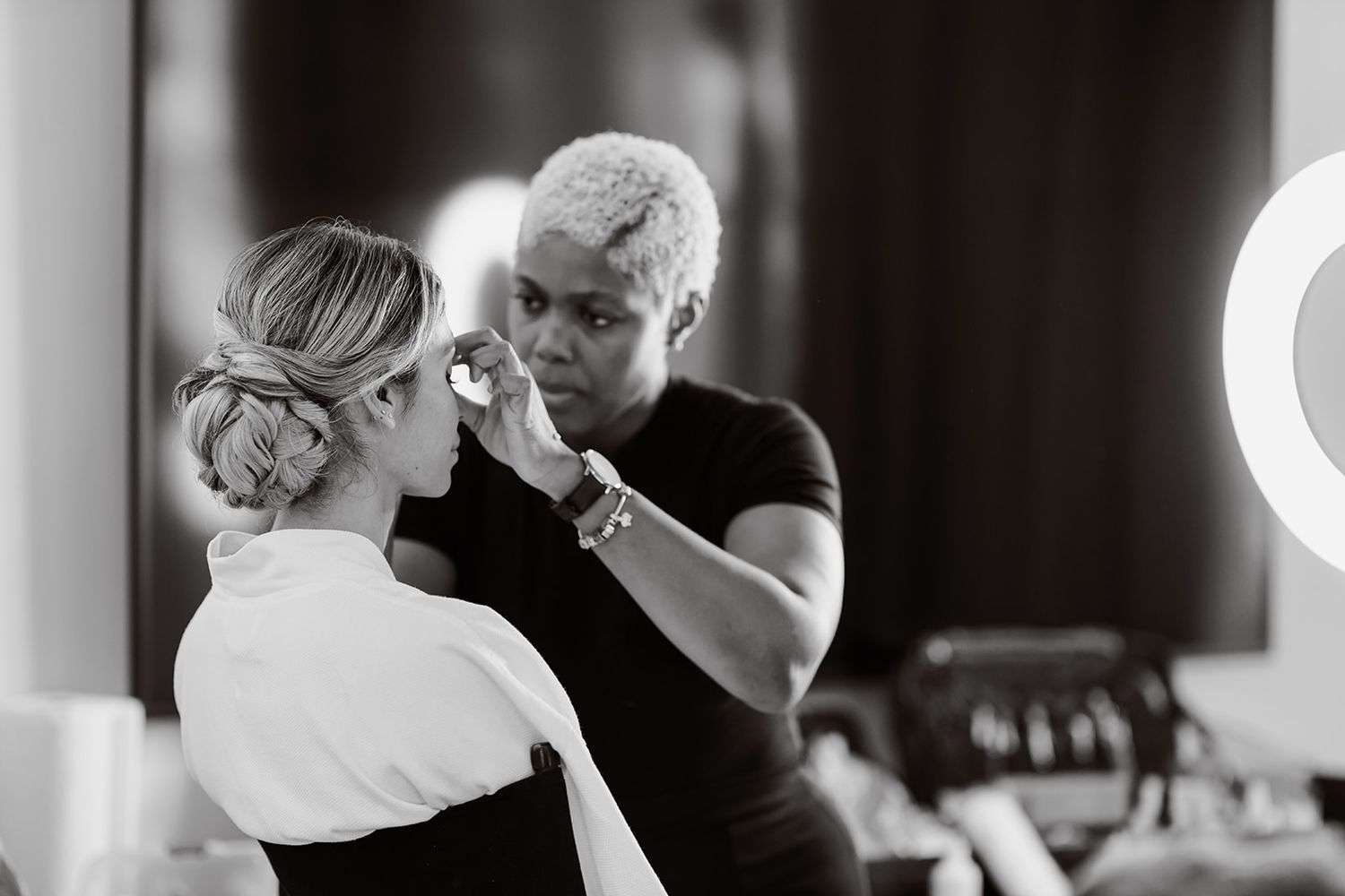 Black and white photo of makeup application during wedding preparation.
