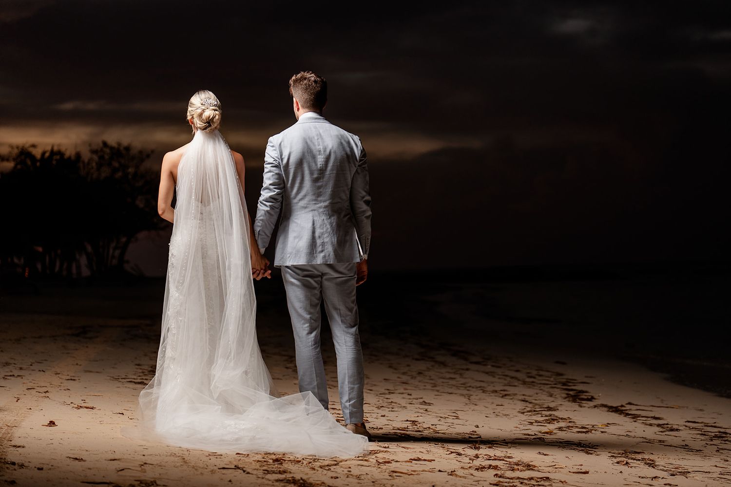 Silhouette of newlyweds standing on beach at sunset with dramatic sky.