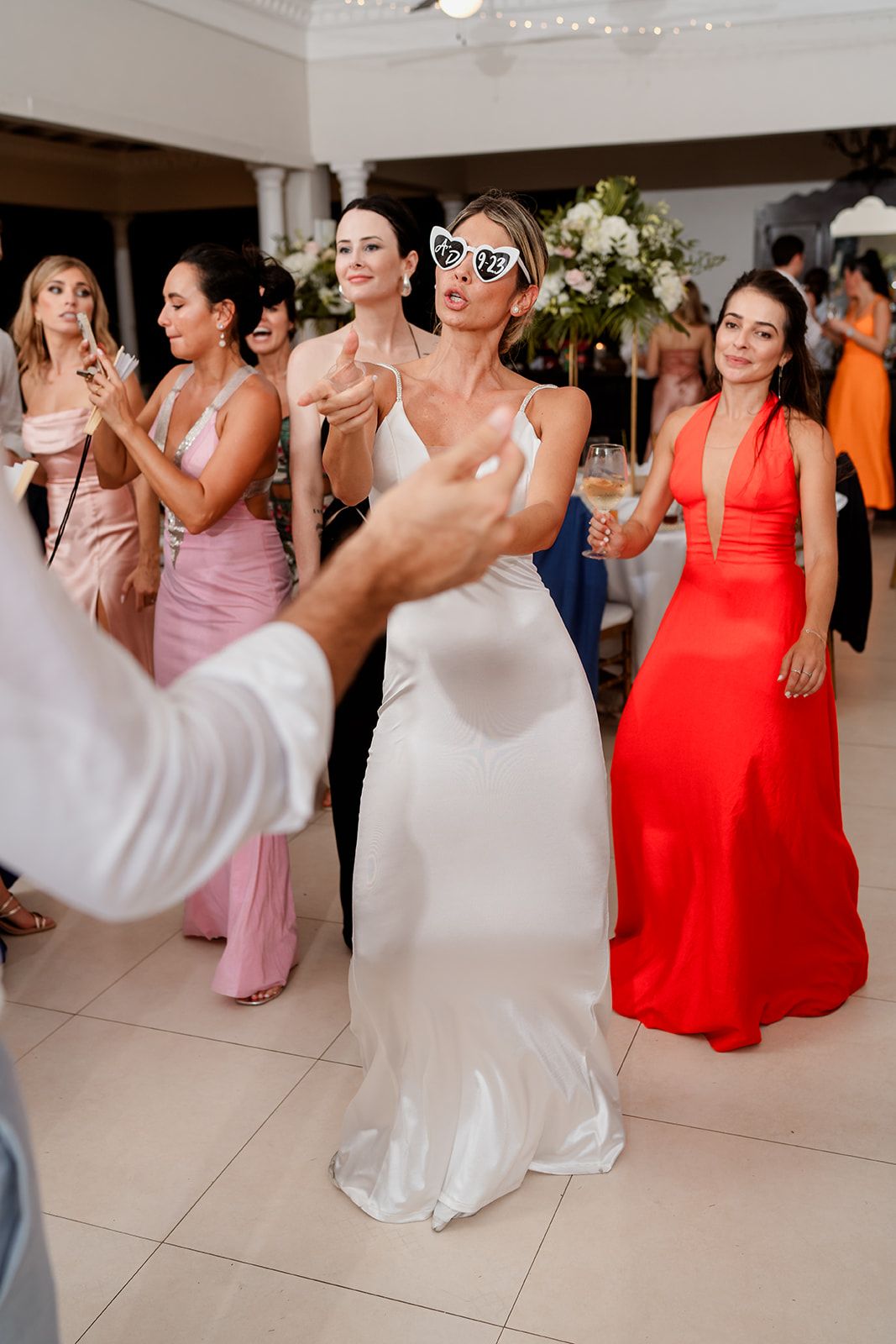 Guests in colorful formal dresses dance and celebrate at an elegant indoor wedding reception.