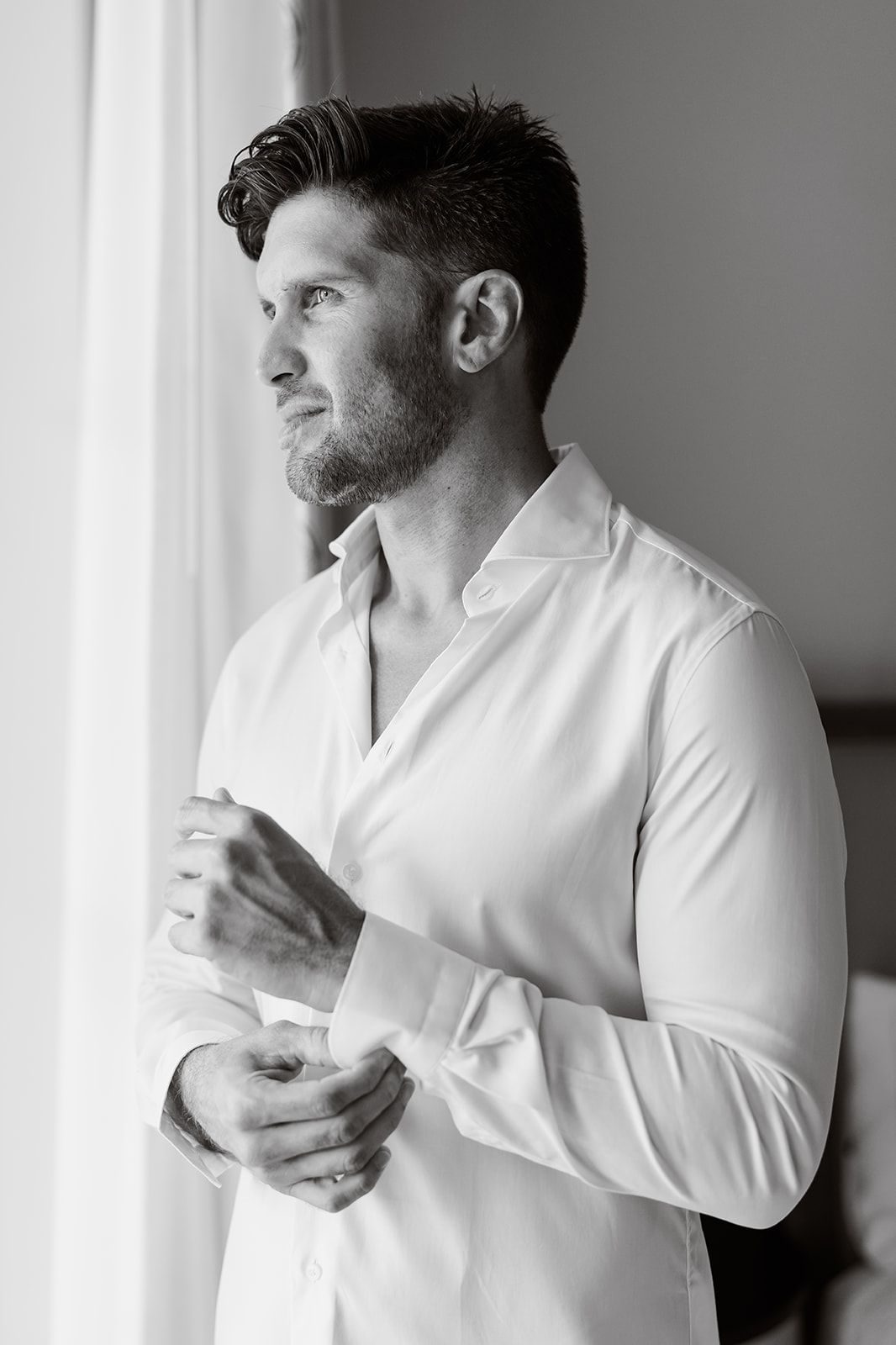 Candid portrait of person in white shirt buttoning cuff while looking to side.
