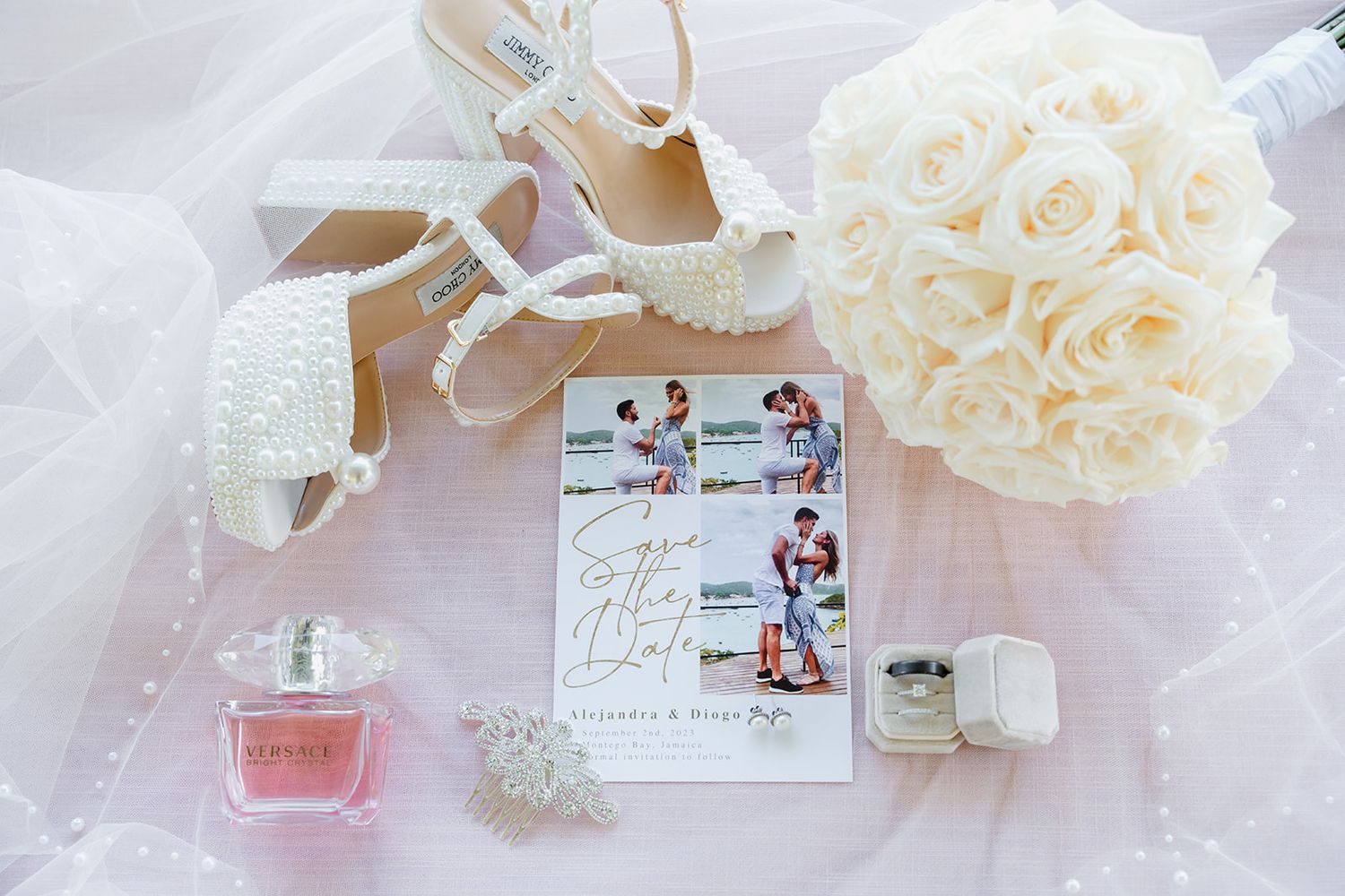 Wedding details flatlay with white shoes, perfume bottle, roses and photos on pink fabric.