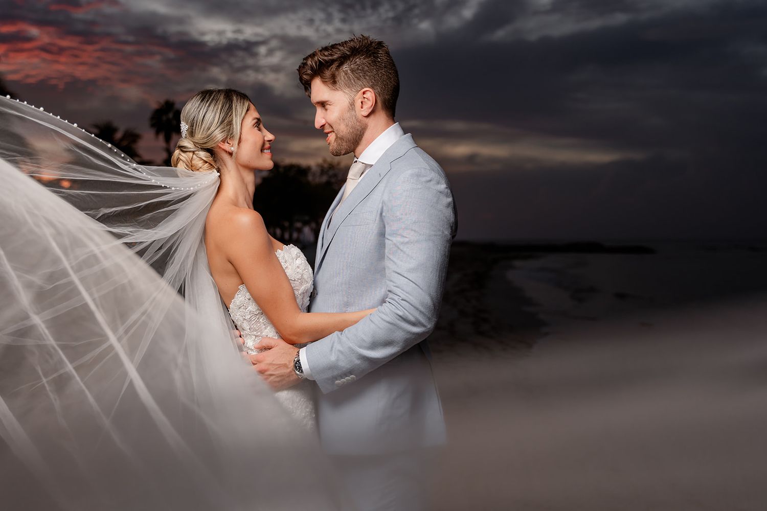 Romantic sunset portrait of newlyweds embracing with dramatic cloudy sky backdrop.