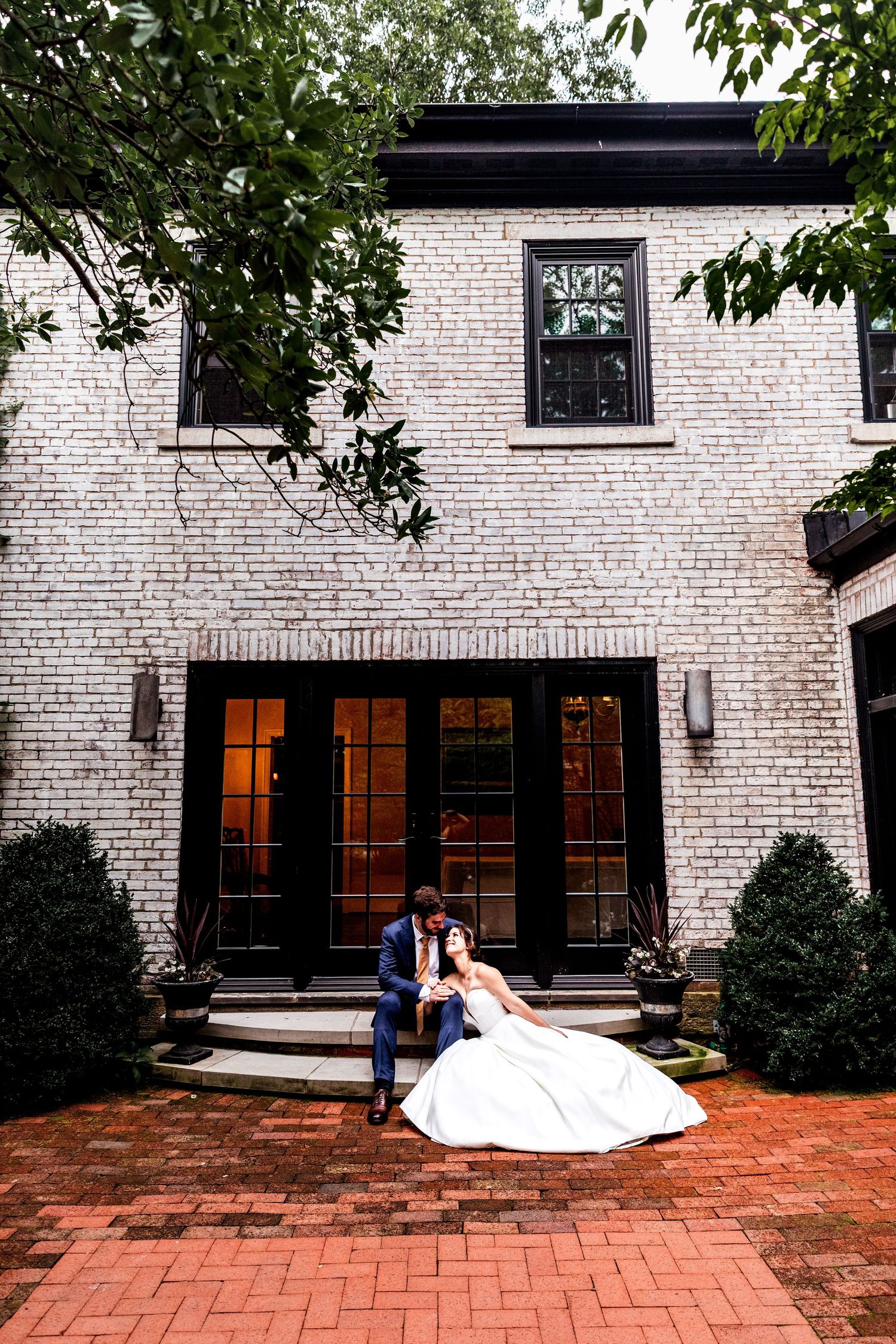 A sequence of four photos showing a couple posing on a brick patio in front of a white brick building with large windows.
