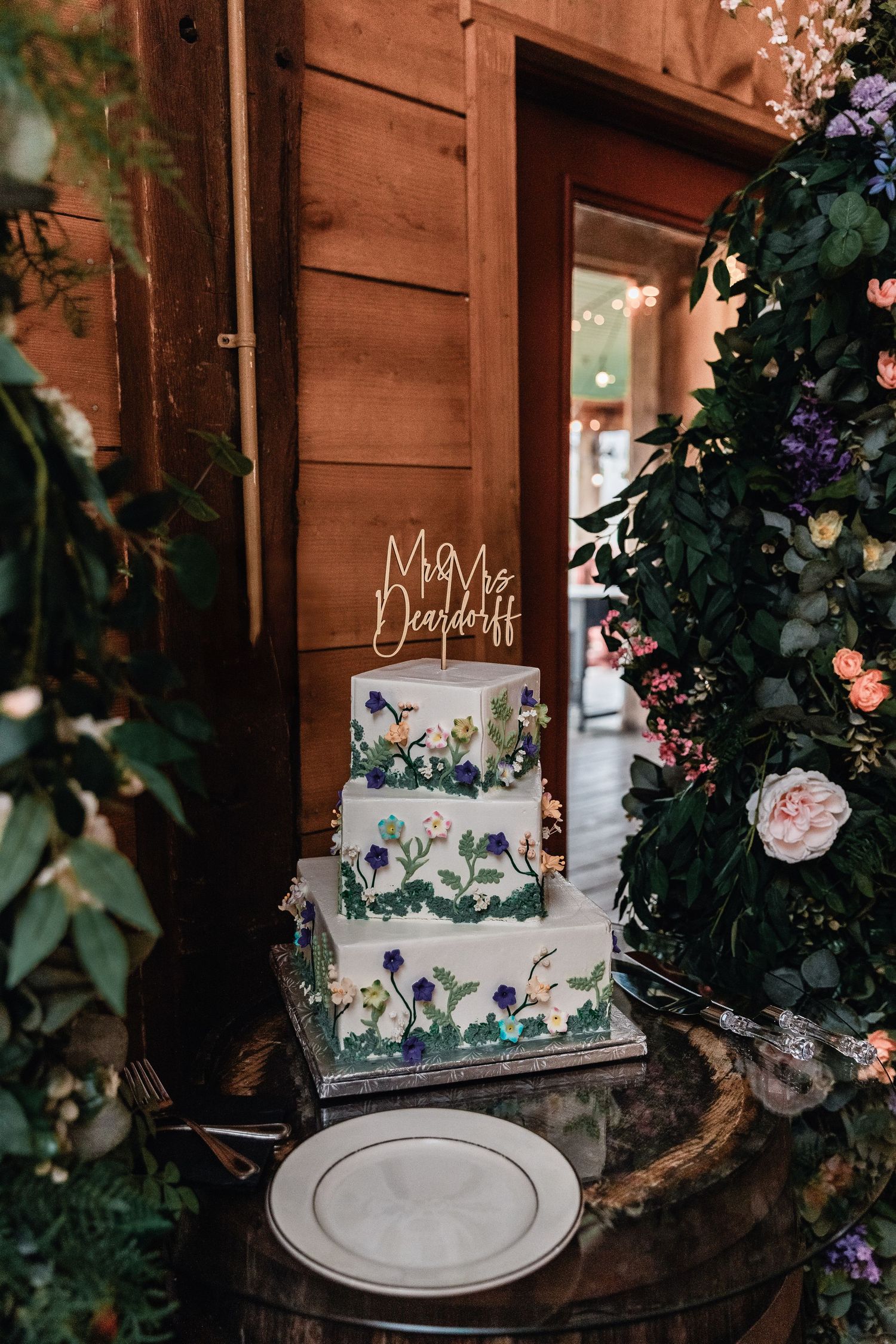 Elegant floral wedding cake with “Mr & Mrs Deardorff” topper at rustic barn wedding reception – wedding photo inspiration