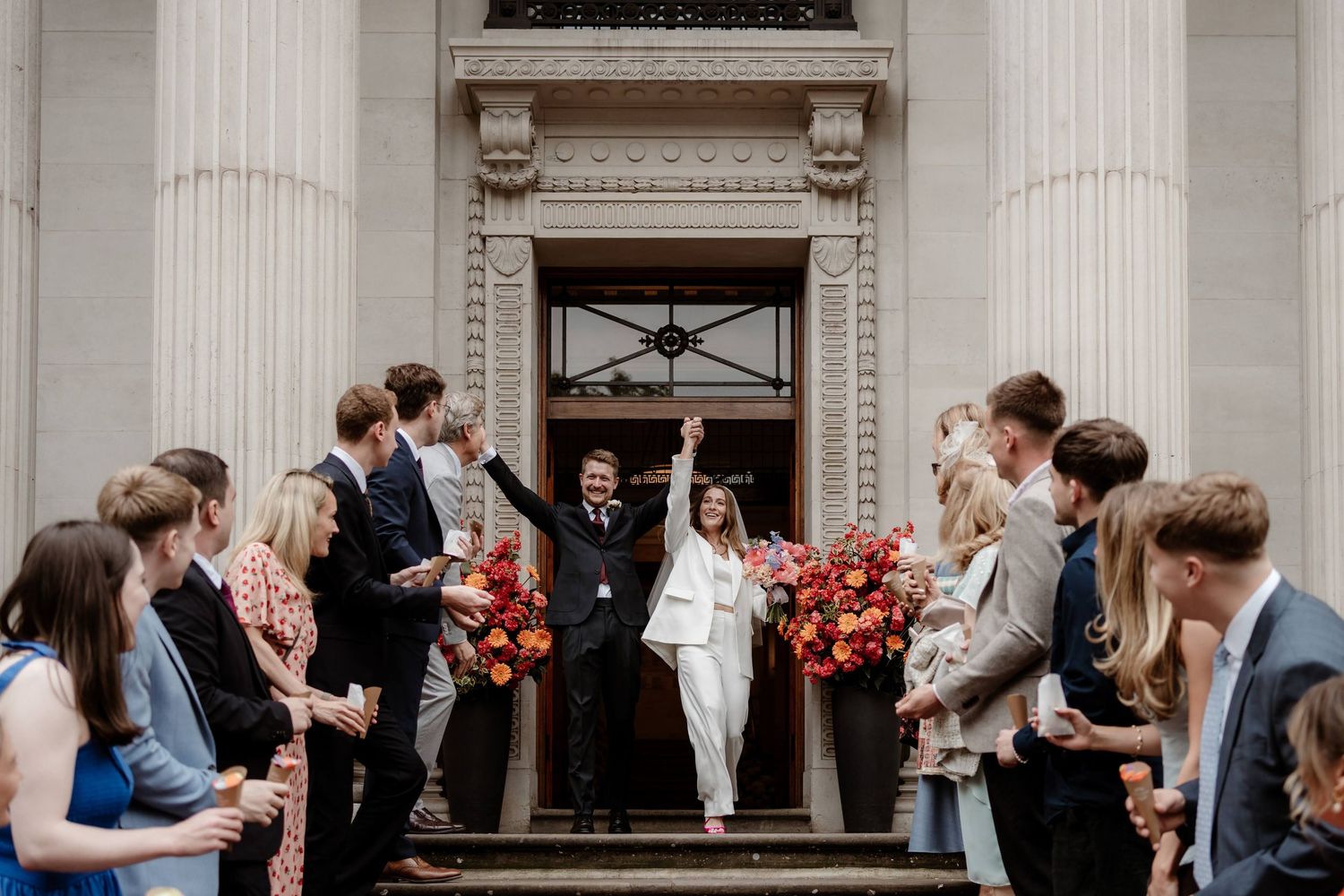 Couple cheers as they walk out of their Old Marylebone Town Hall London Wedding into a confetti tunnel.