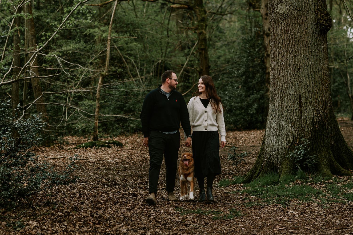 Two people sharing an intimate moment while walking together in a wooded forest area during autumn.
