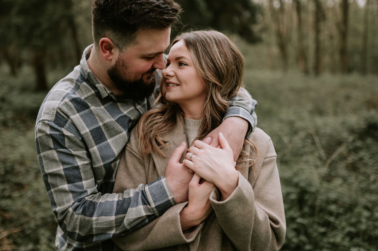 A couple embraces tenderly in a natural outdoor setting wearing casual sweaters on a moody autumn day.