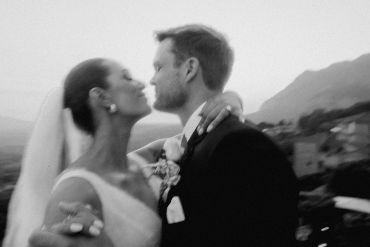 Romantic black and white wedding portrait of a couple embracing against a mountain landscape backdrop.