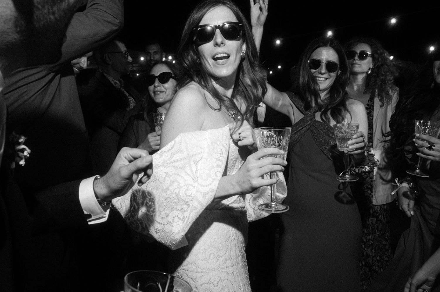 Wedding party celebration with guests wearing sunglasses and enjoying drinks at night.