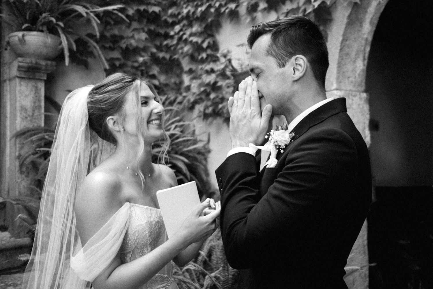 Black and white wedding moment captured outdoors against an ivy-covered stone archway.