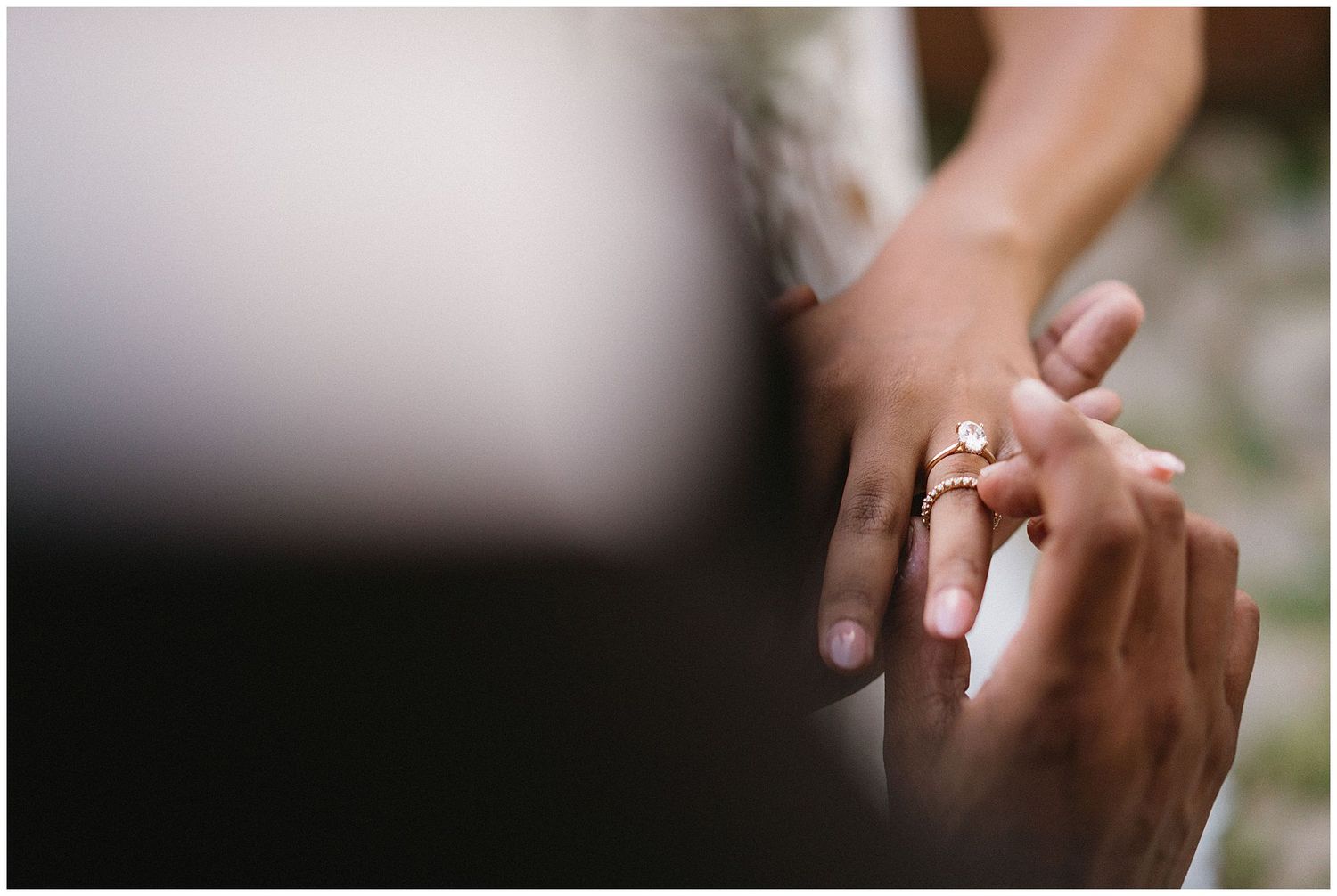 Close-up photo of hands placing an engagement ring with sparkling diamonds on a finger during a special moment.