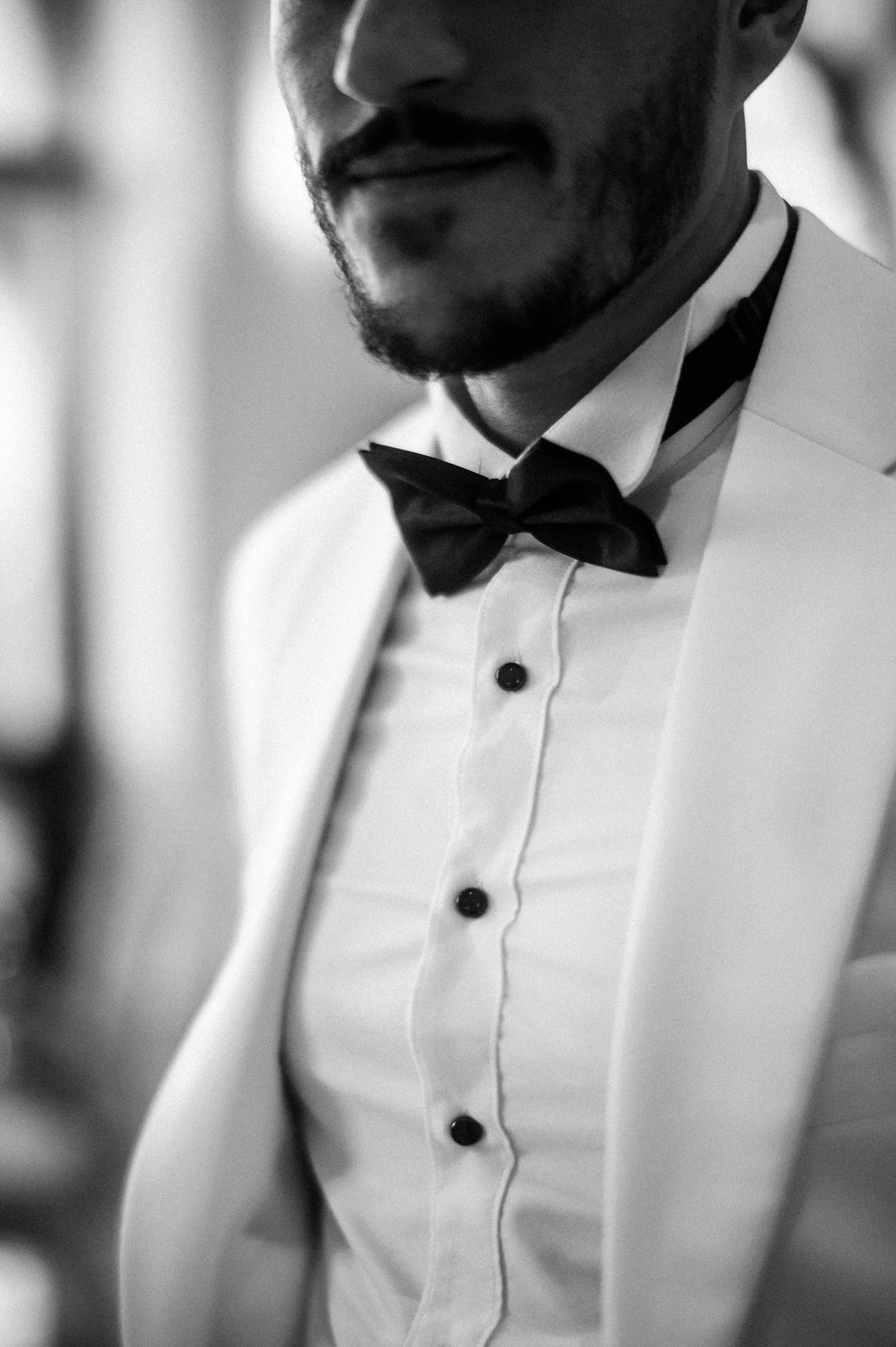 Close-up black and white photo showing details of tuxedo with crisp white shirt, black bowtie and jacket lapel.