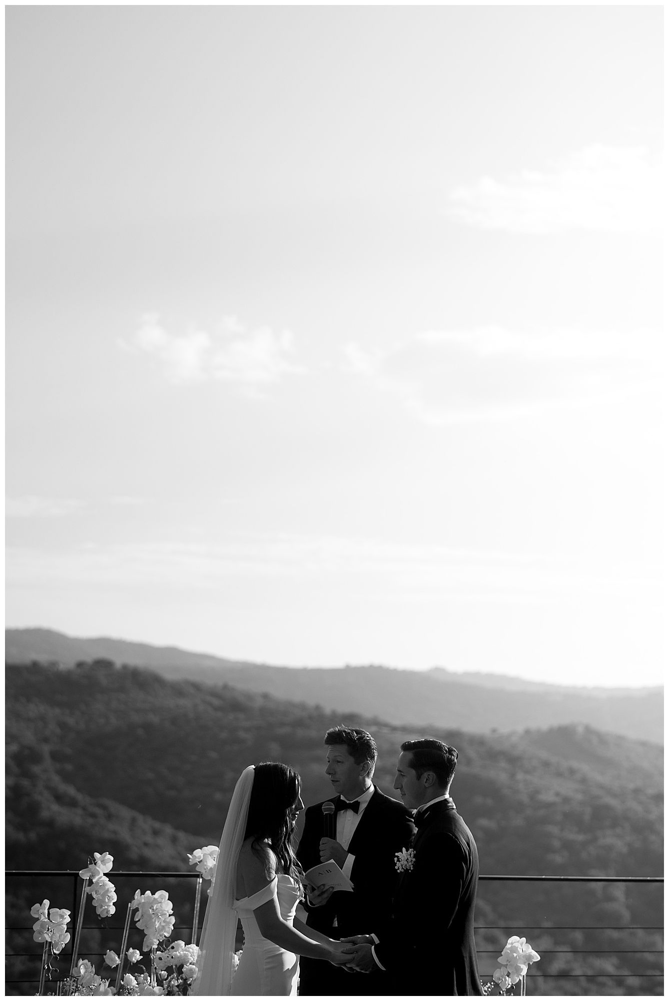 A black and white panoramic scene of people standing outdoors against a mountain backdrop on a cloudy day.