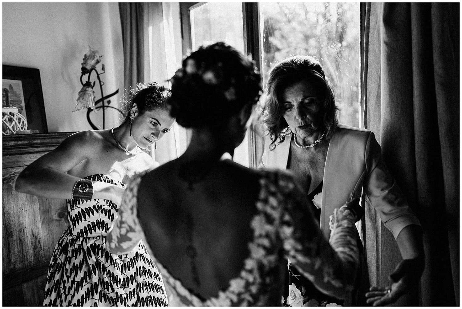 A black and white photograph shows a person looking at their reflection in a vanity mirror lit by natural window light.