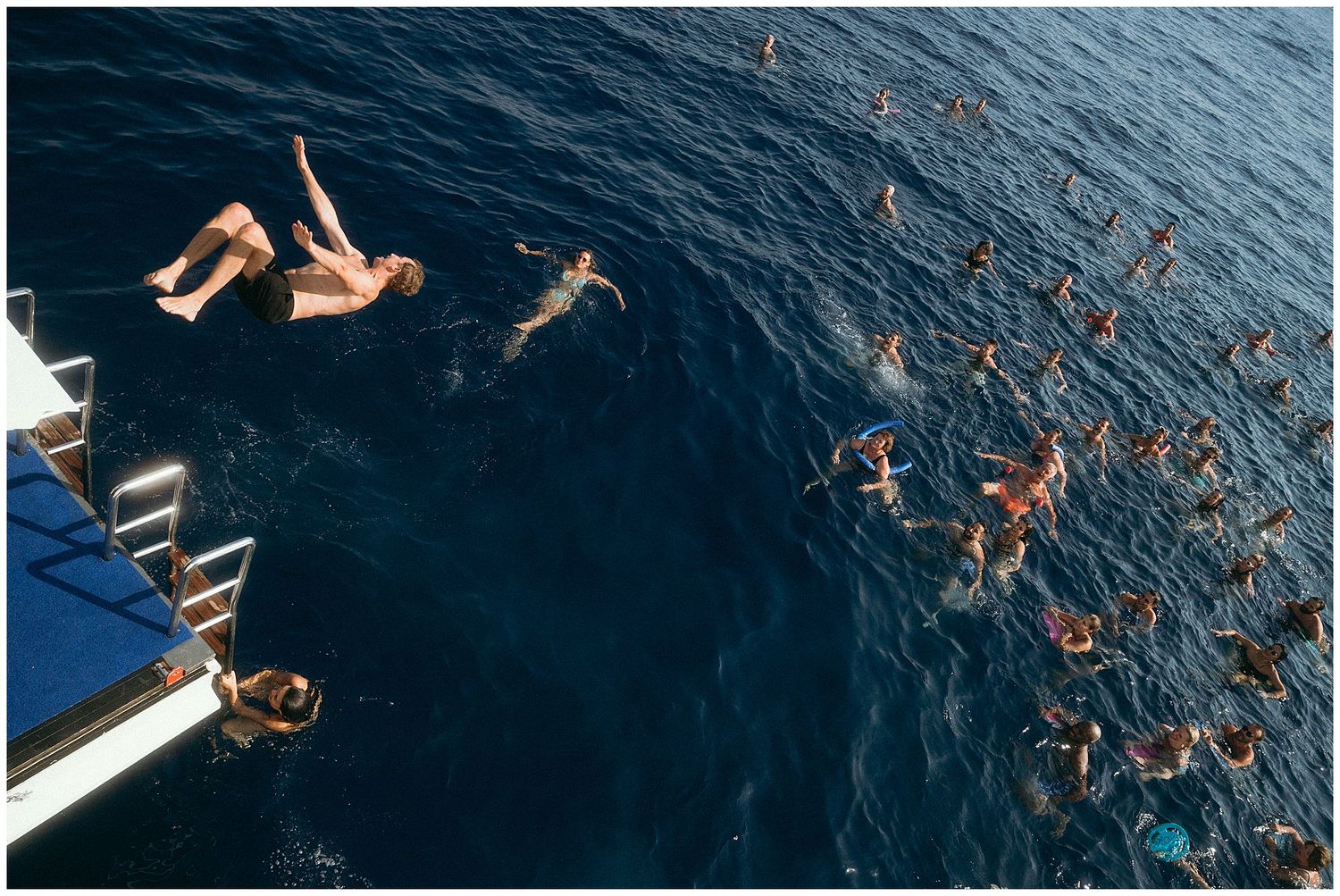 People swimming and jumping into deep blue ocean water from a platform during a summer activity.