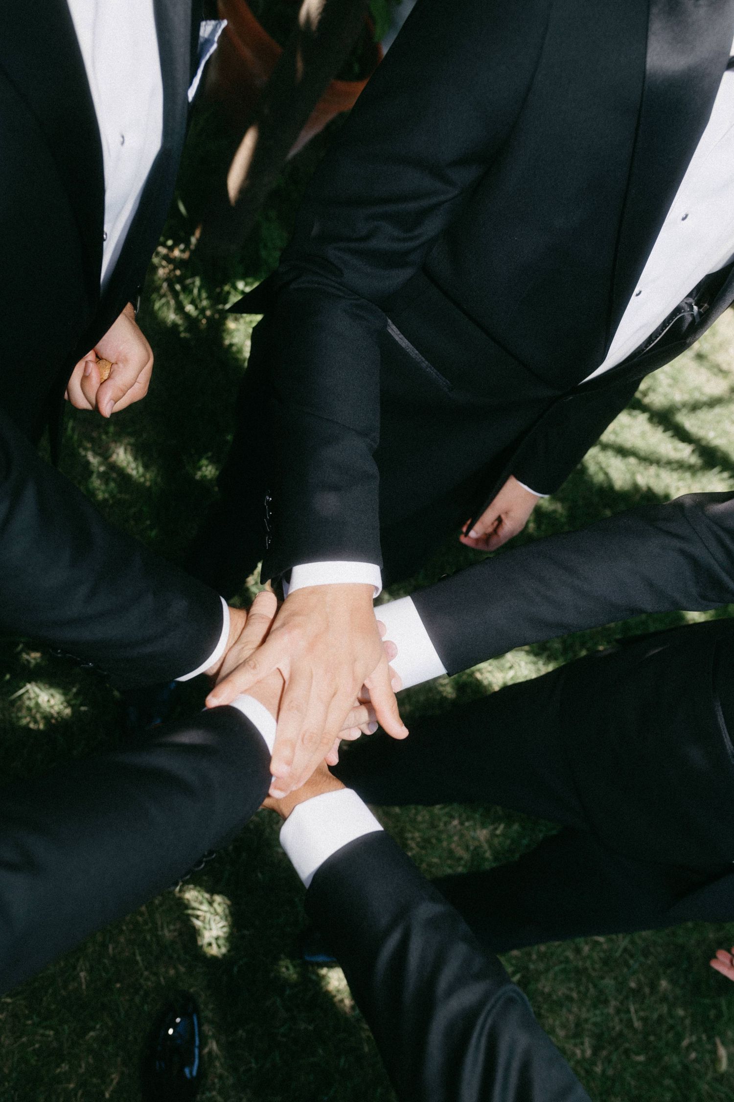 Multiple hands in black suits join together in a circle, showing unity and celebration at a formal event.
