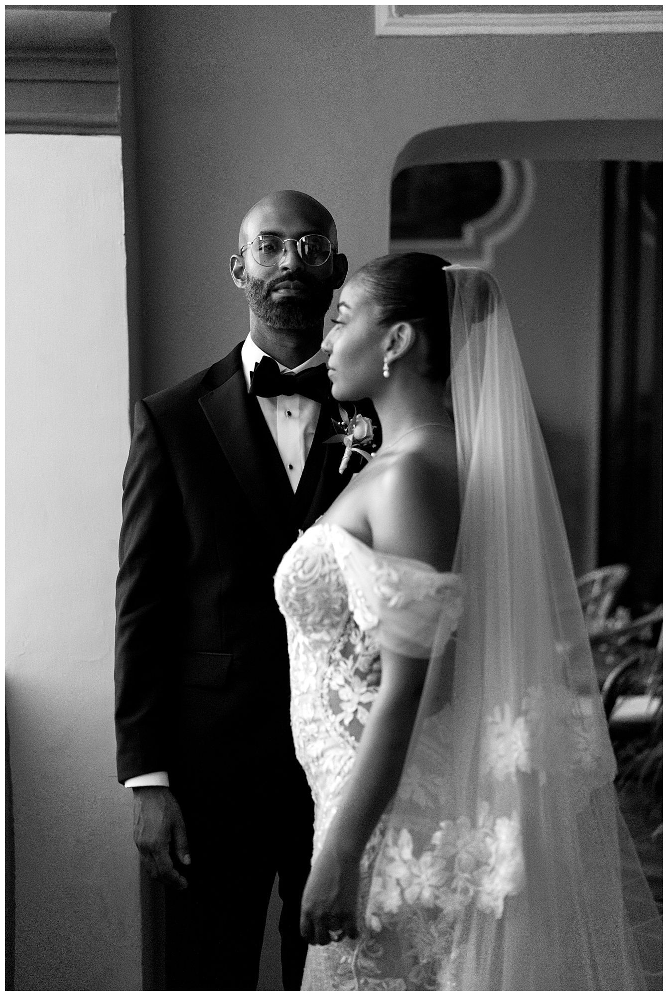 A black and white wedding photograph showing a couple in formal attire, with the bride wearing a lace dress and veil.
