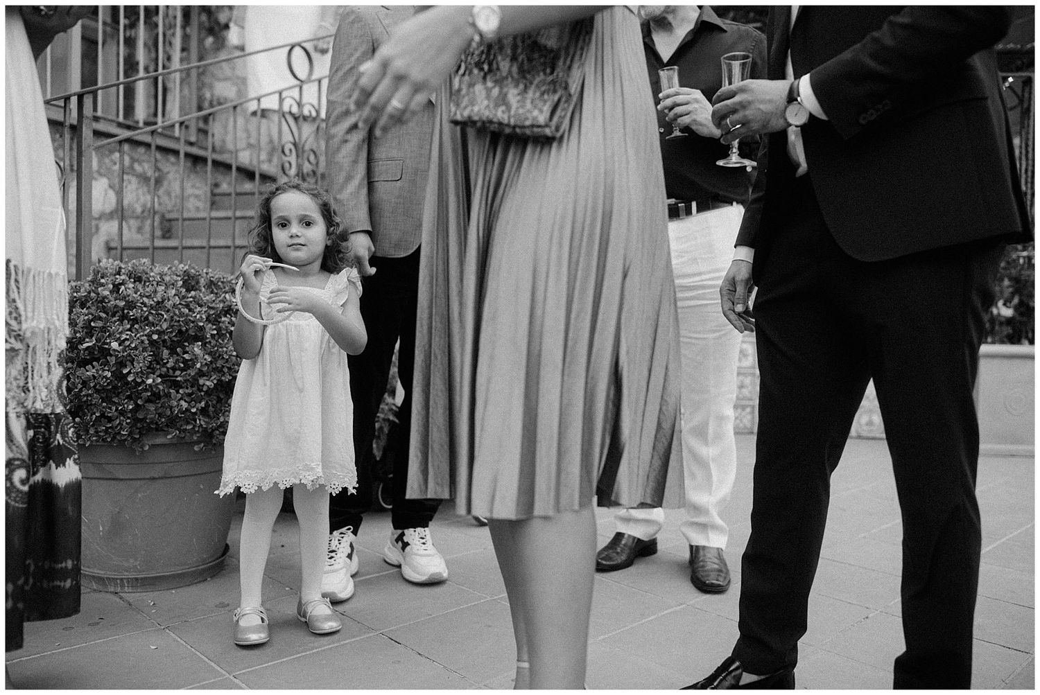 A child stands in a white dress next to adults, with a street scene and buildings visible in black and white photograph.