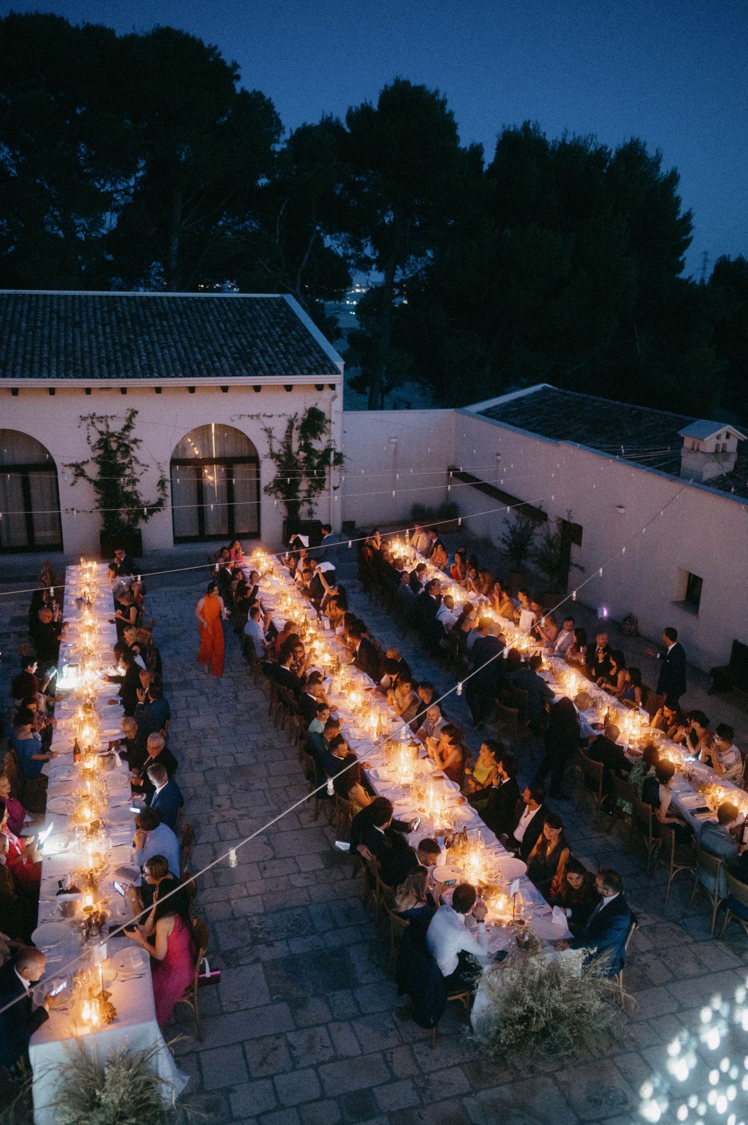 Elegant outdoor wedding reception with three long illuminated dining tables arranged in parallel at dusk under string lights.