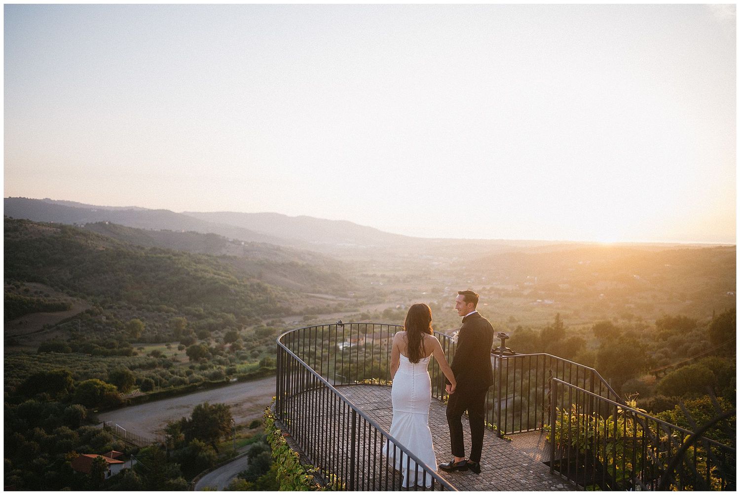 Scenic mountain landscape view at golden sunset hour with silhouetted iron railing overlooking rolling hills.