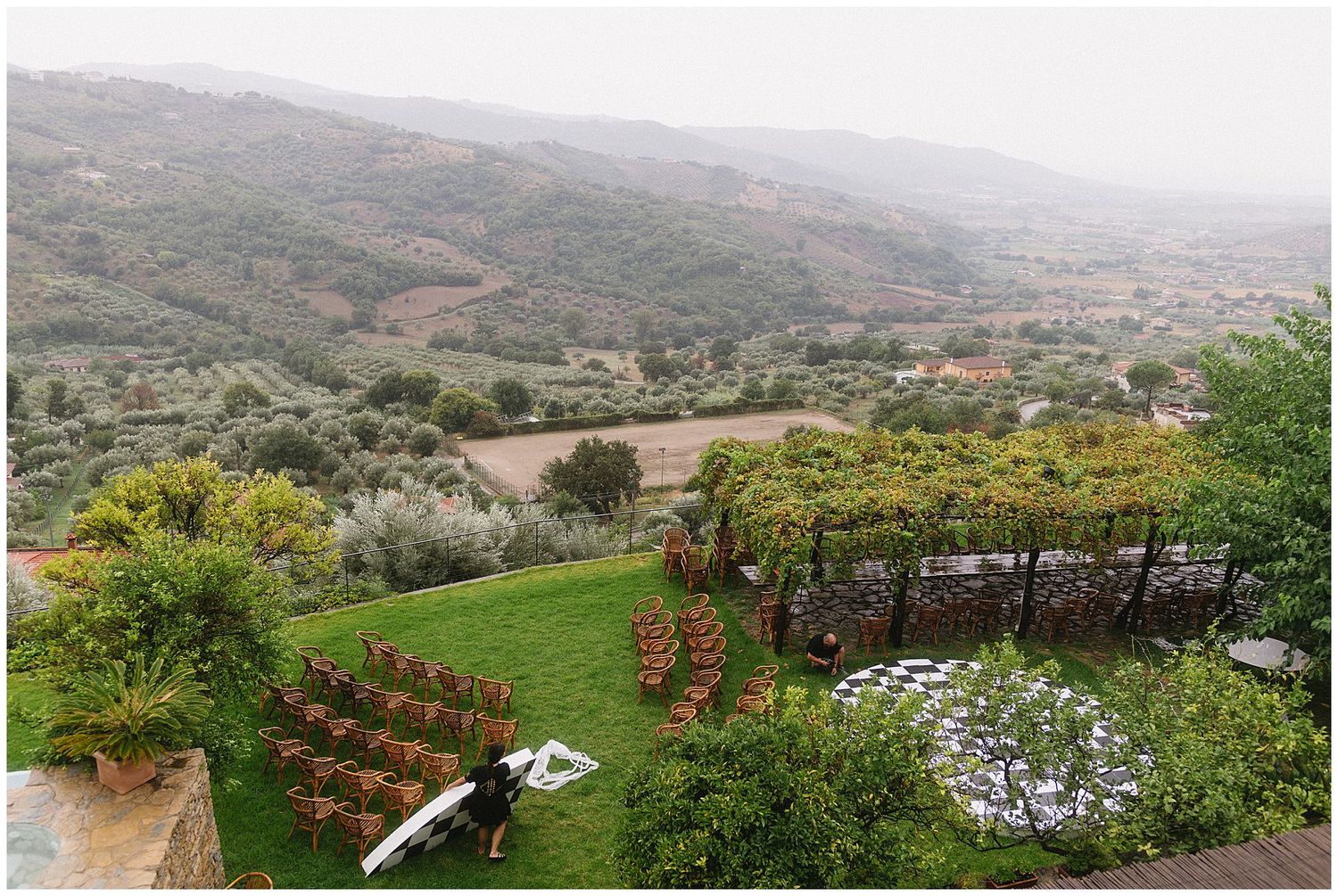 Lush hillside garden terrace overlooking a scenic Tuscan valley with olive groves and patterned landscaping.