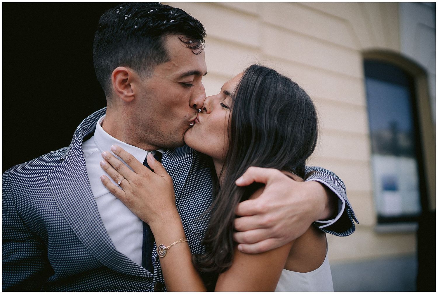 A romantic close-up photo of a couple sharing an intimate kiss outside a building.