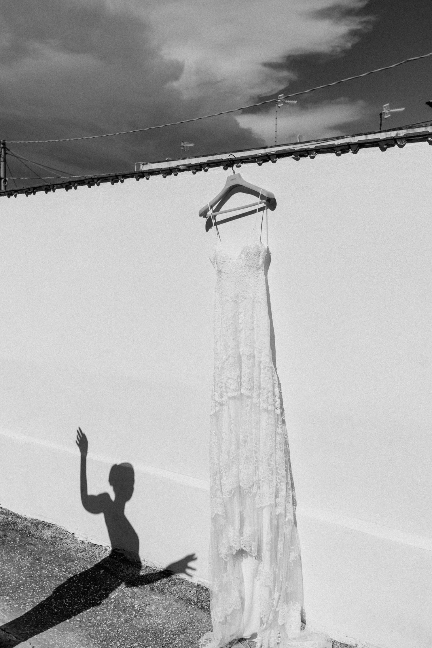 A white wedding dress hanging against a wall with a shadow of someone reaching up towards it.
