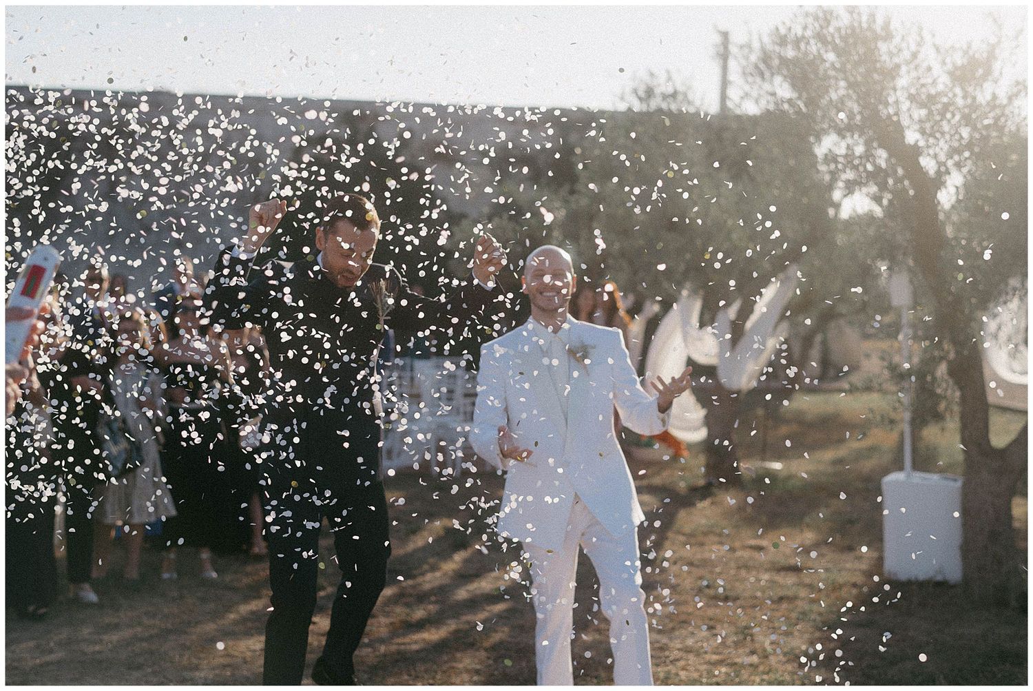 Couple celebrating with confetti on a sunny day surrounded by trees, creating a dreamy outdoor atmosphere.