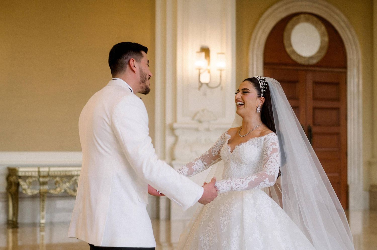A joyful couple shares a romantic moment together in an elegant venue with white walls and ornate details.