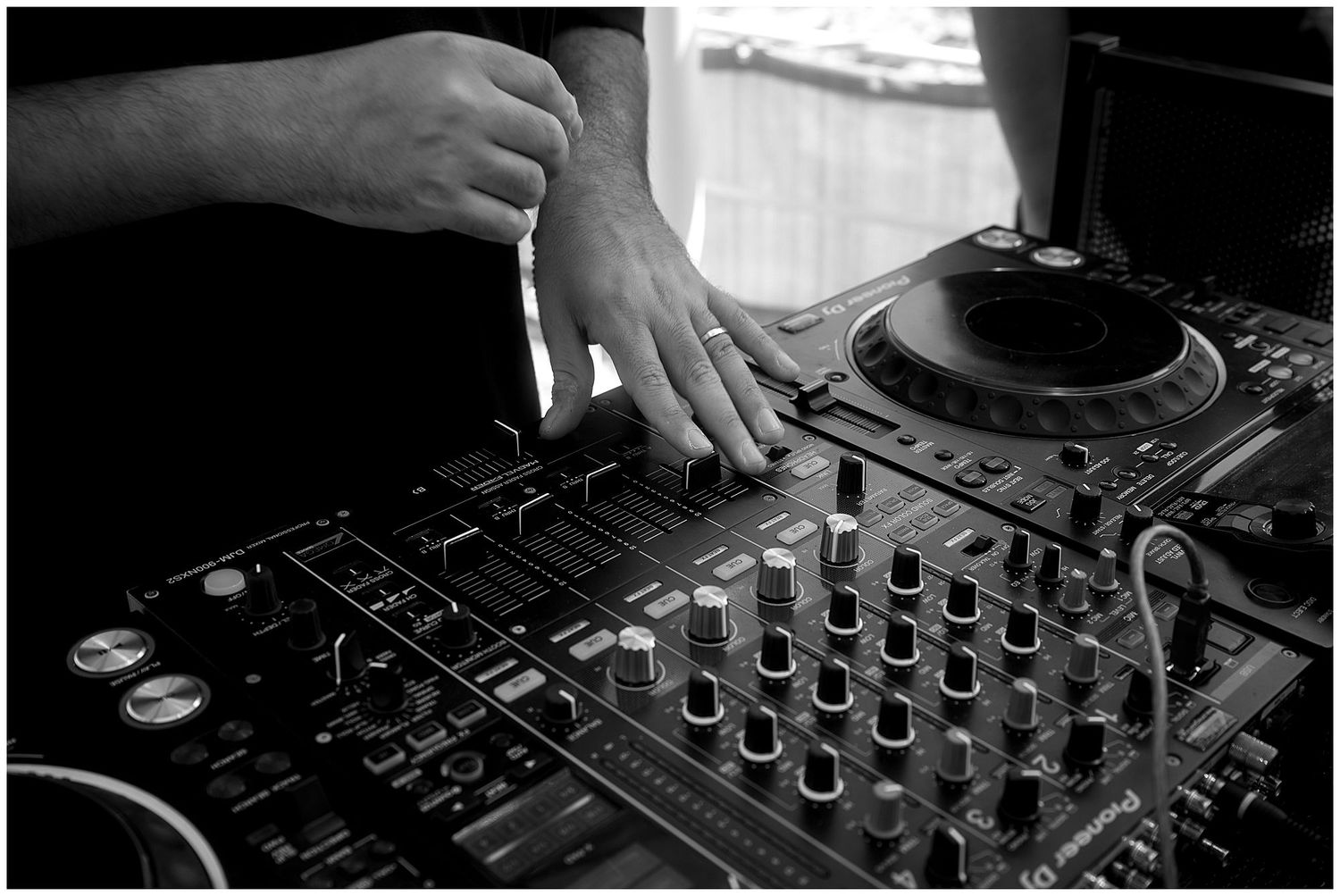 Close-up black and white shot of hands operating a professional DJ mixer with turntables and control knobs.
