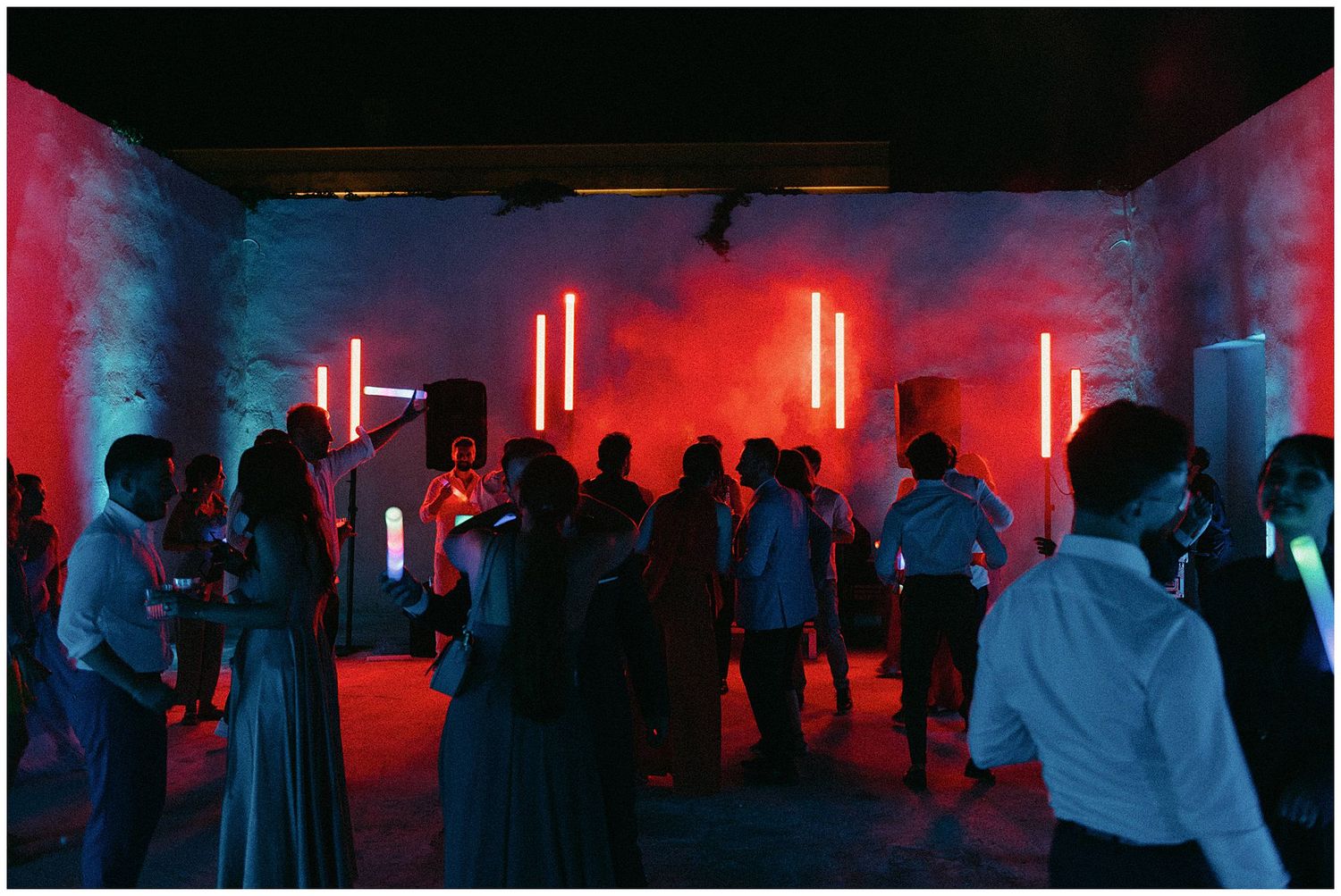 A dim nightclub scene lit with glowing red neon lights as people dance and socialize in a crowded space.